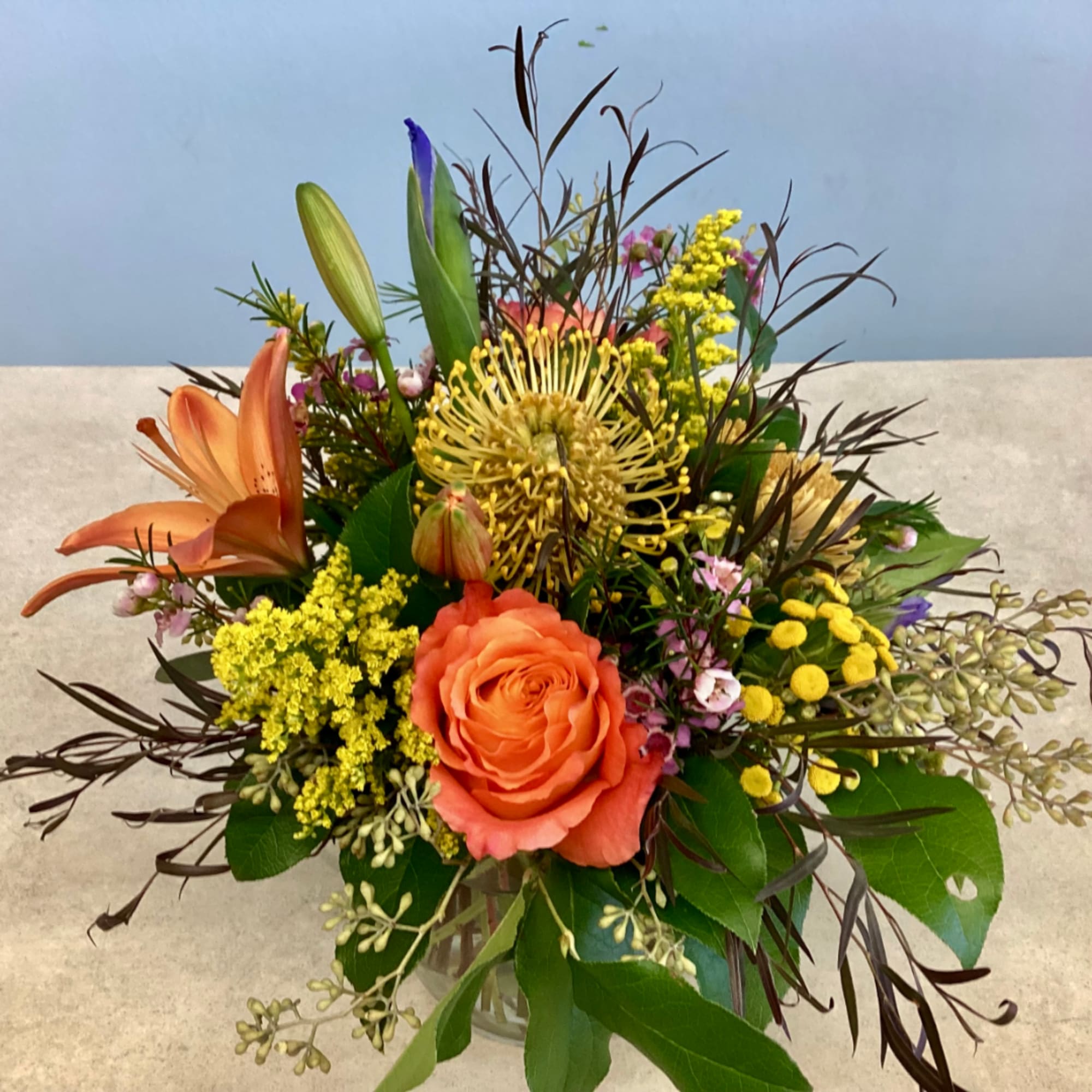 Orange rose and lily bouquet in a clear vase with yellow accents