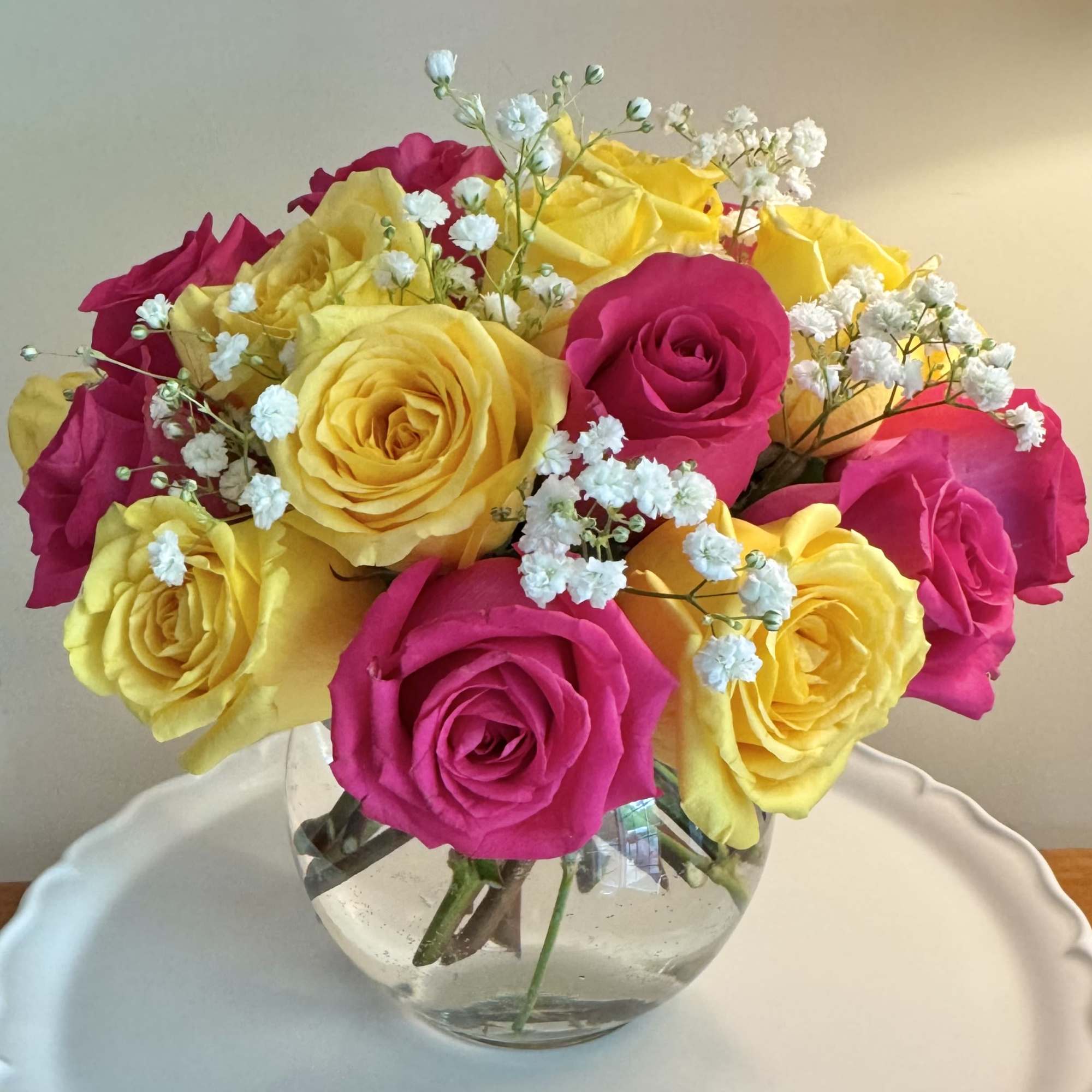 A lovely bowl of 24 colorful roses and filler brightens and lifts