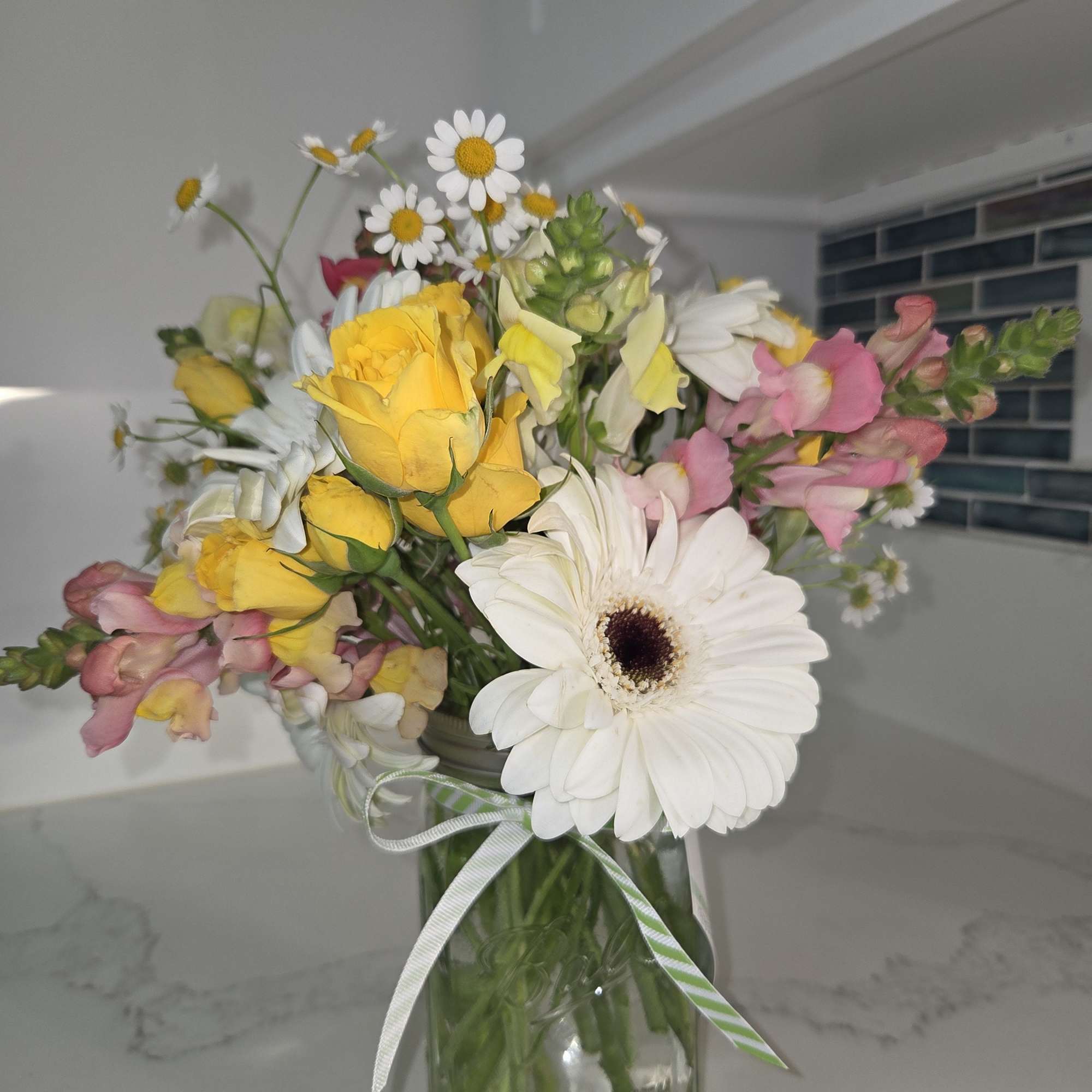 Mixed bouquet in a glass vase with yellow roses, white daisies, and pink snapdragons