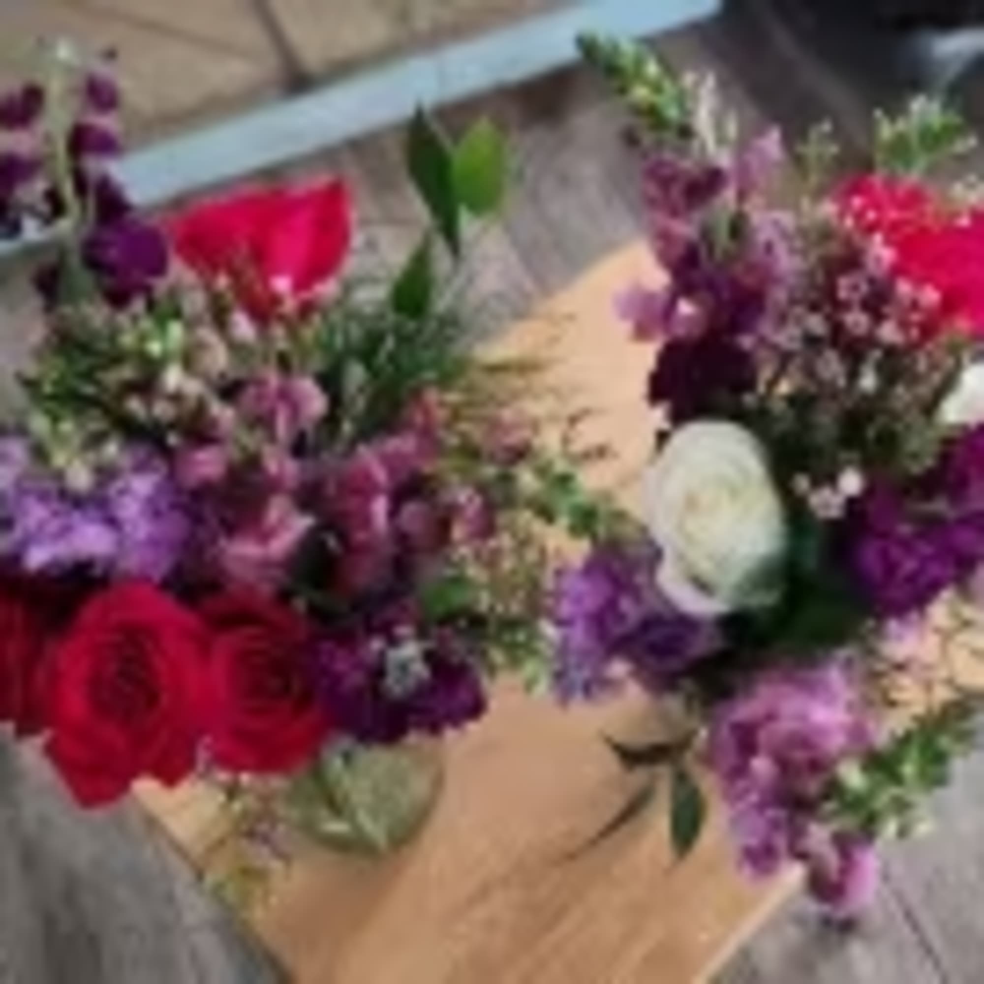 Two mixed bouquets with red, purple, and white flowers on a wooden surface