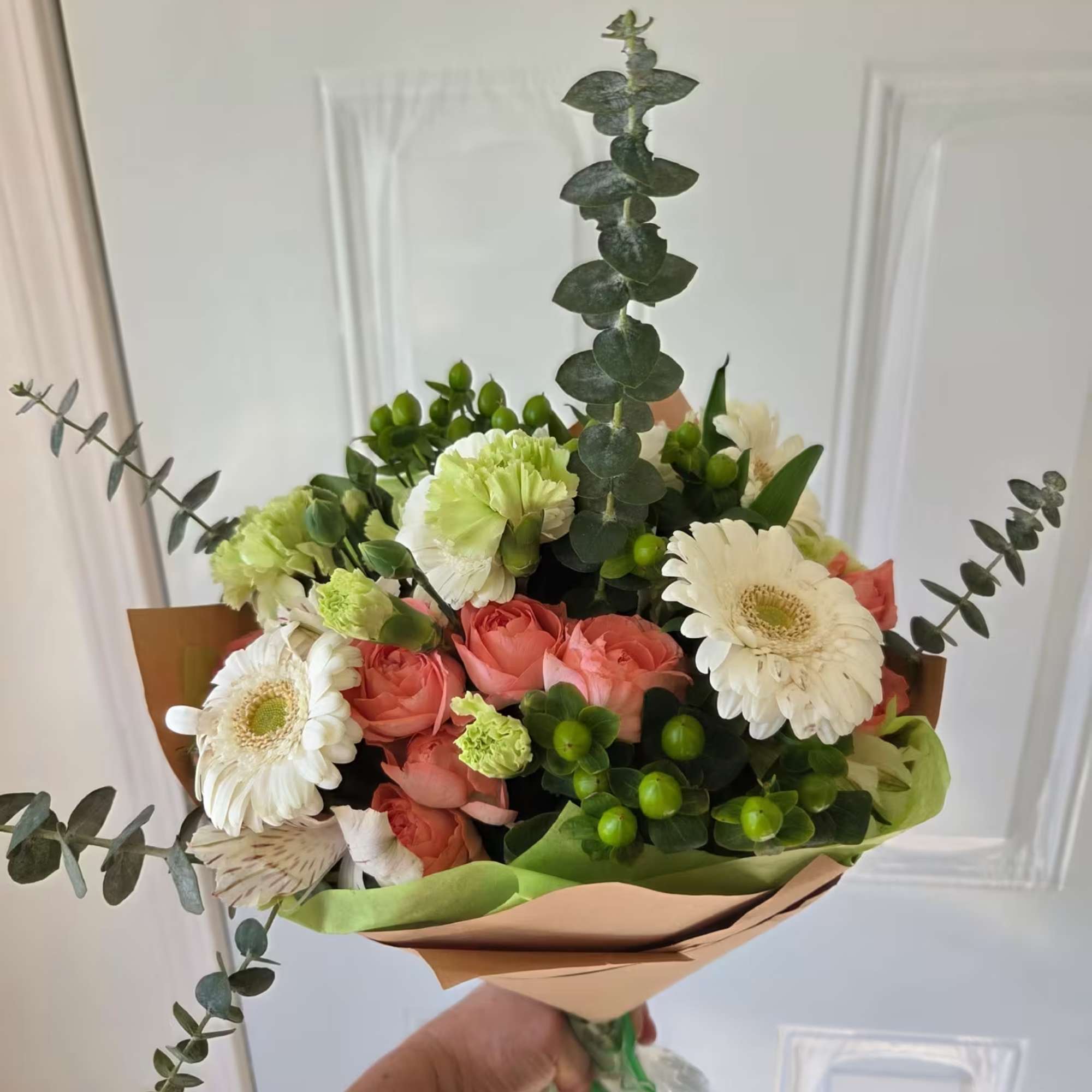 Handheld bouquet of coral roses, white gerbera daisies, and green carnations