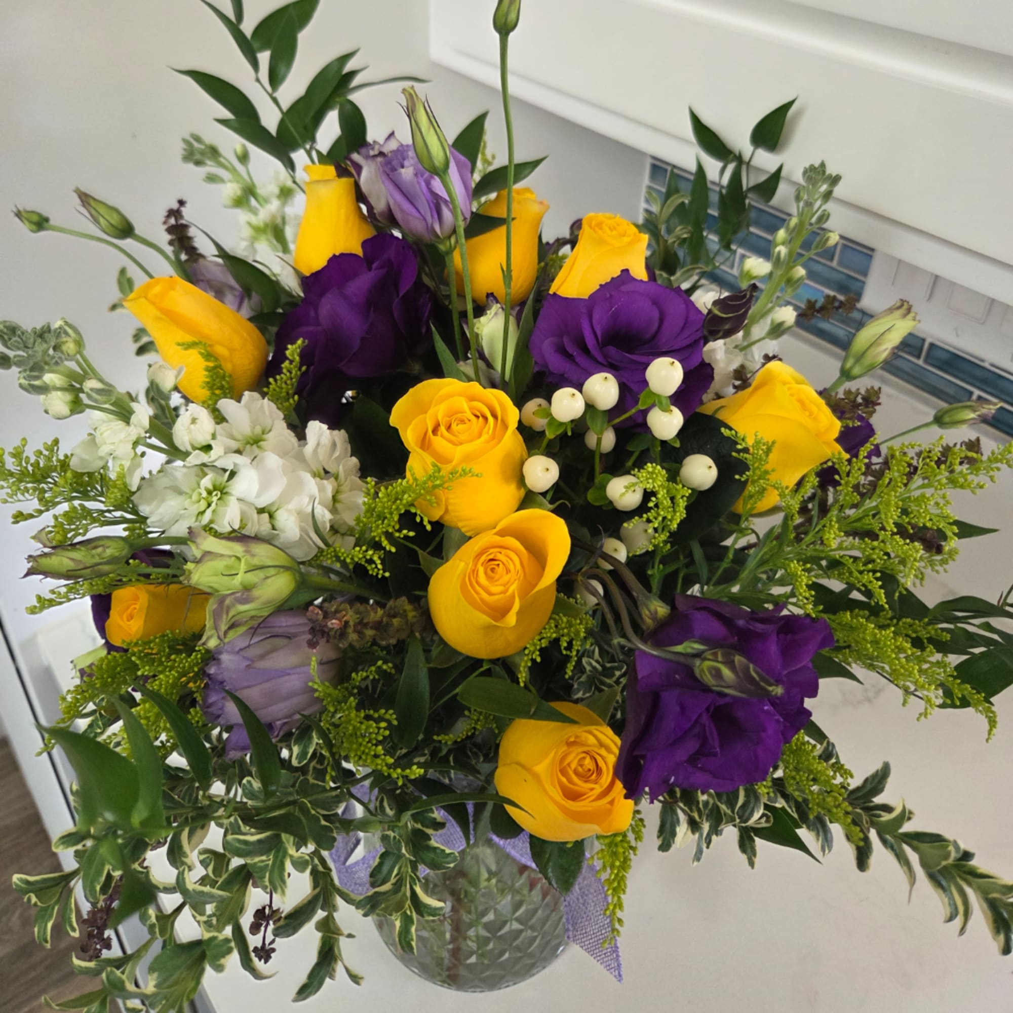 Yellow roses and purple lisianthus in a glass vase