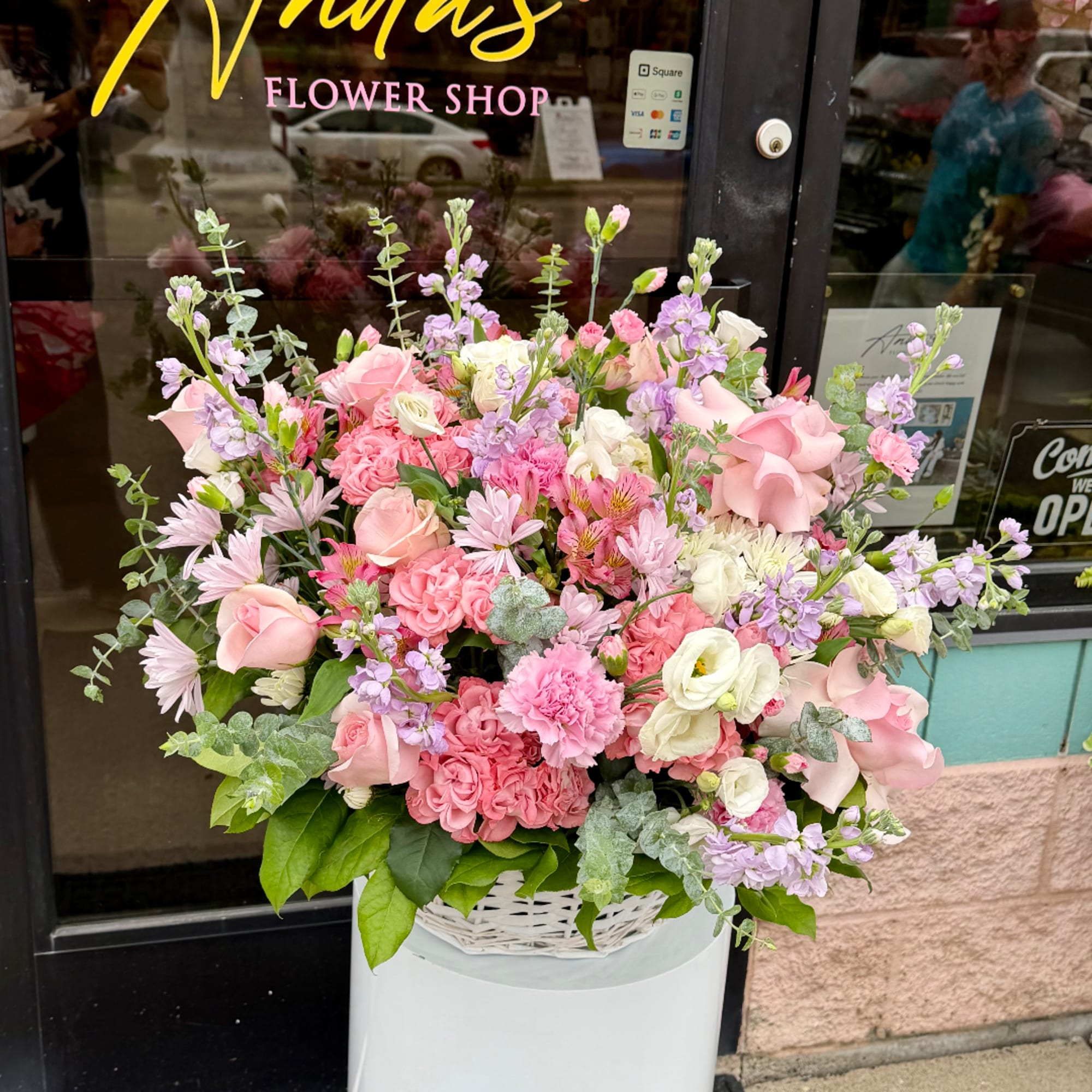 Large pastel flower arrangement in a white basket outside a shop