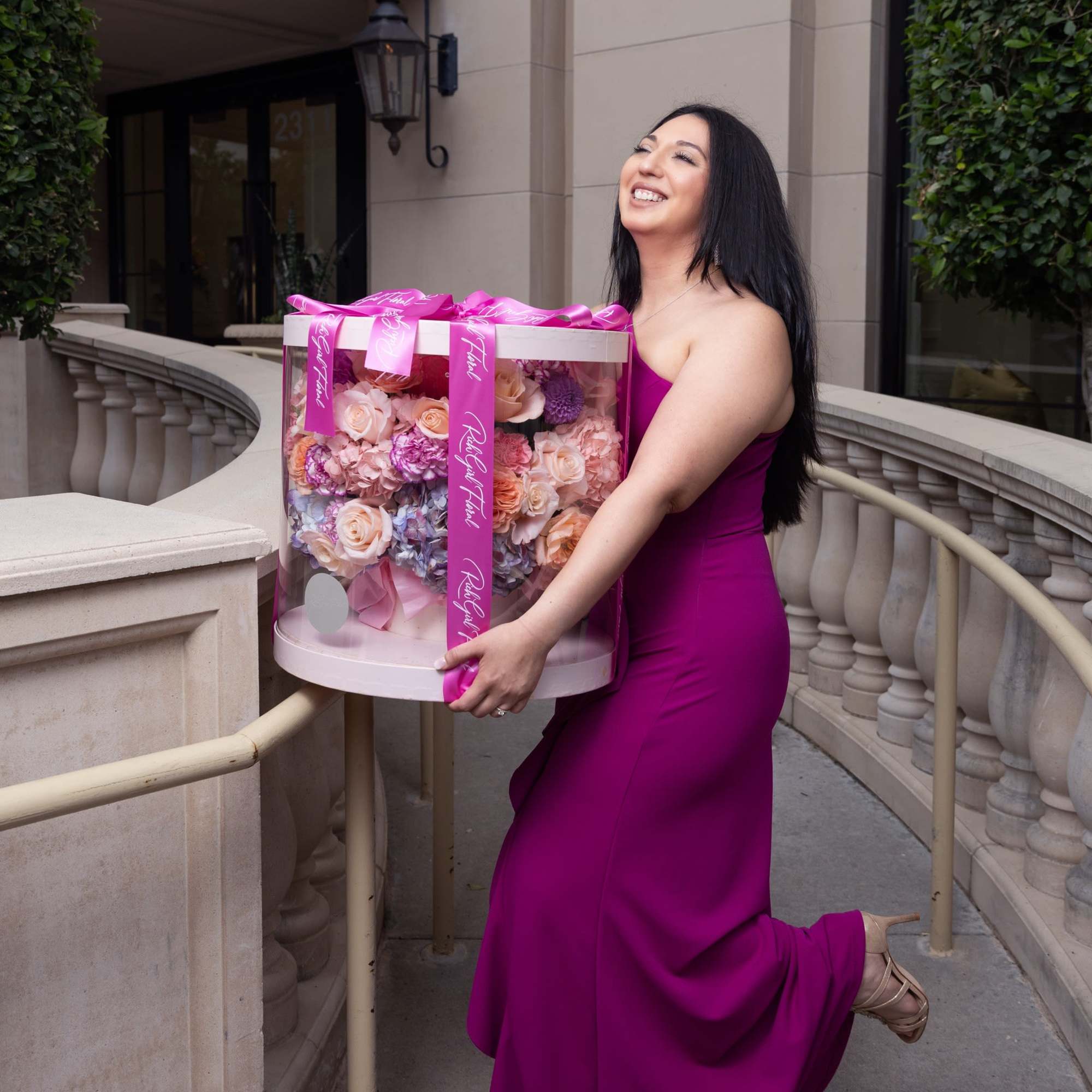 Woman in a magenta dress holding a large round box of pastel flowers