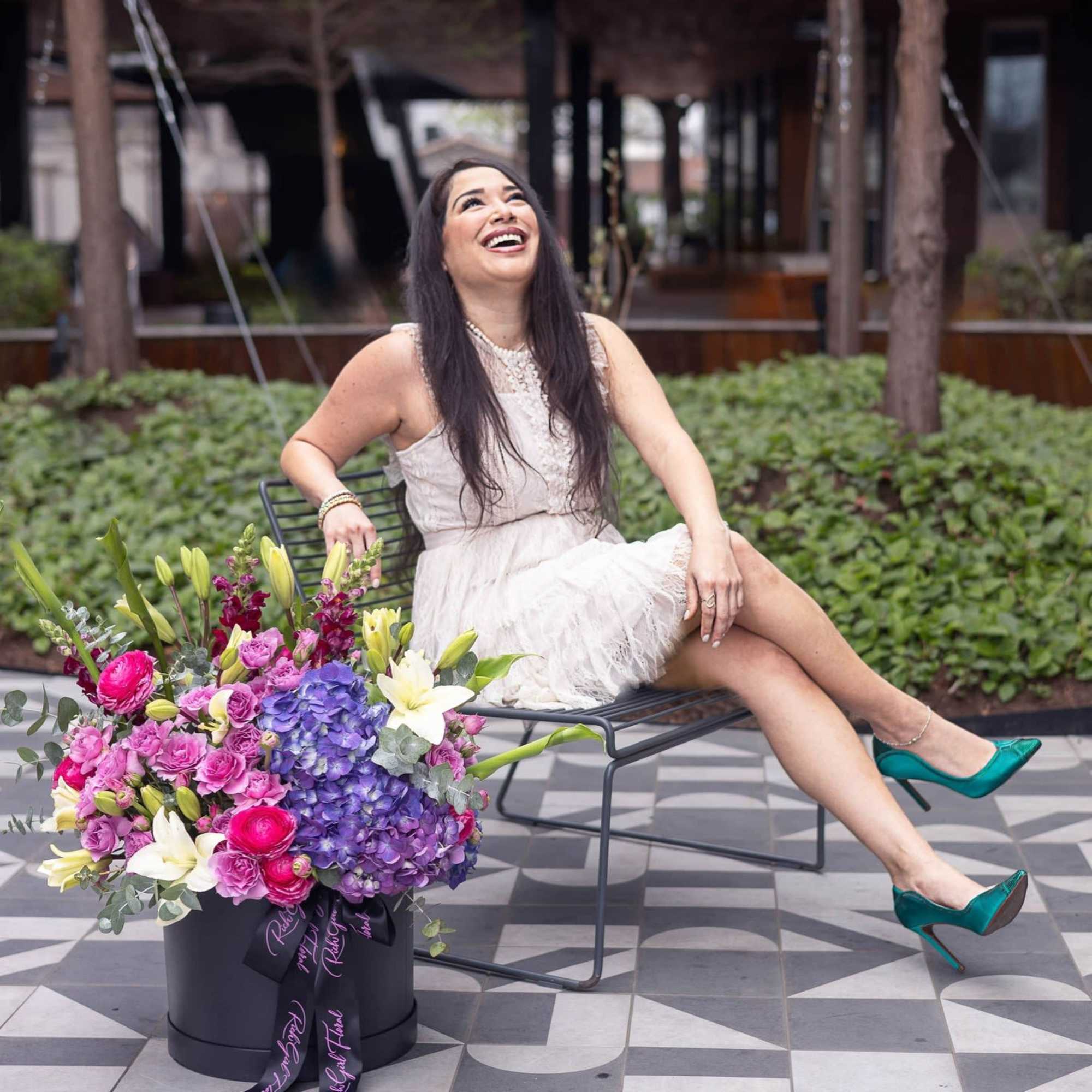 Woman seated beside a large colorful flower arrangement in a black hatbox