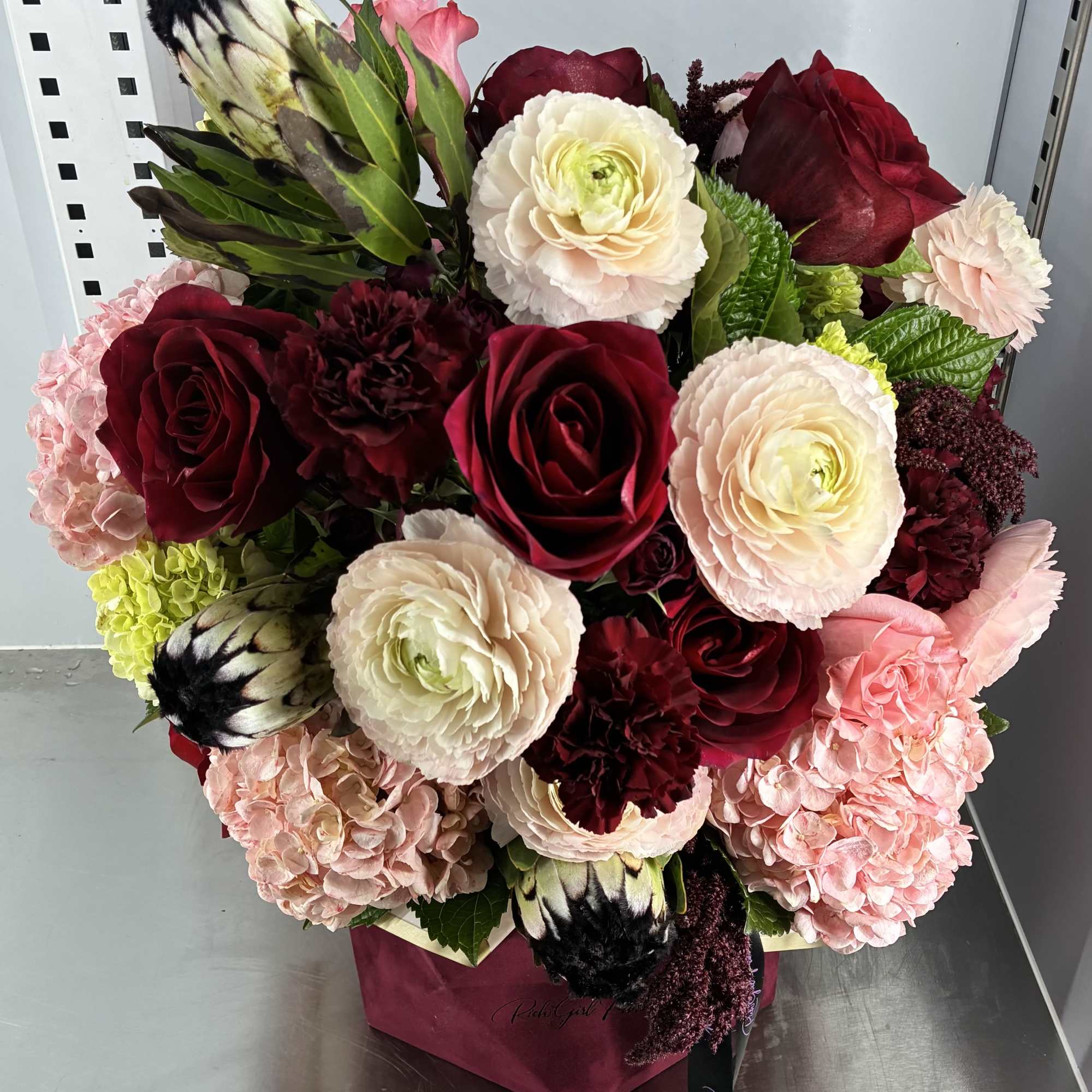 Bouquet of red roses, pale ranunculus, and pink hydrangeas in a box