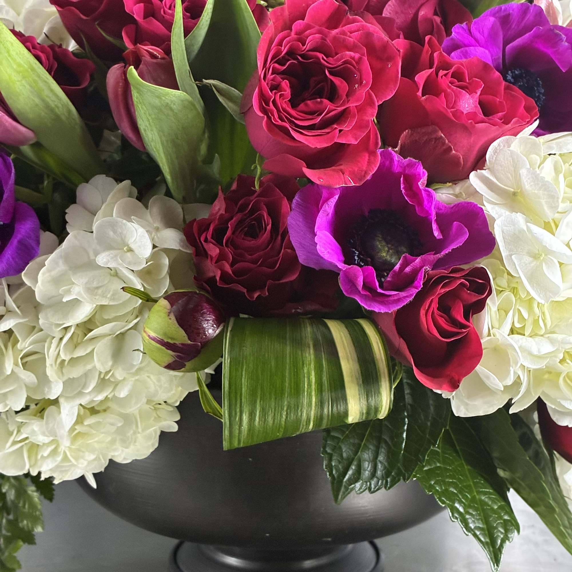 Bouquet of red roses, purple anemones, and white hydrangeas in a black vase