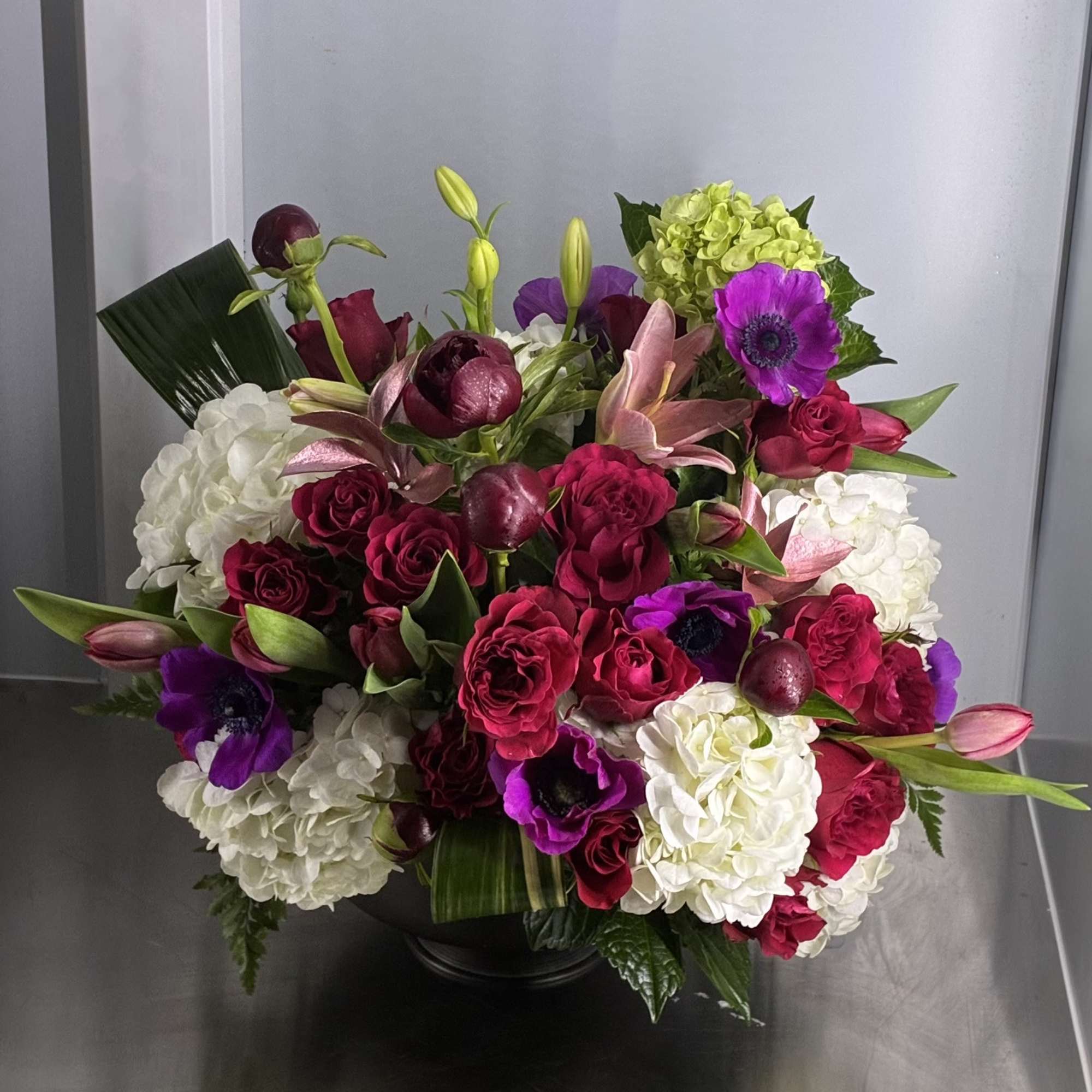 Bouquet of red roses, white hydrangeas, and purple anemones in a black vase