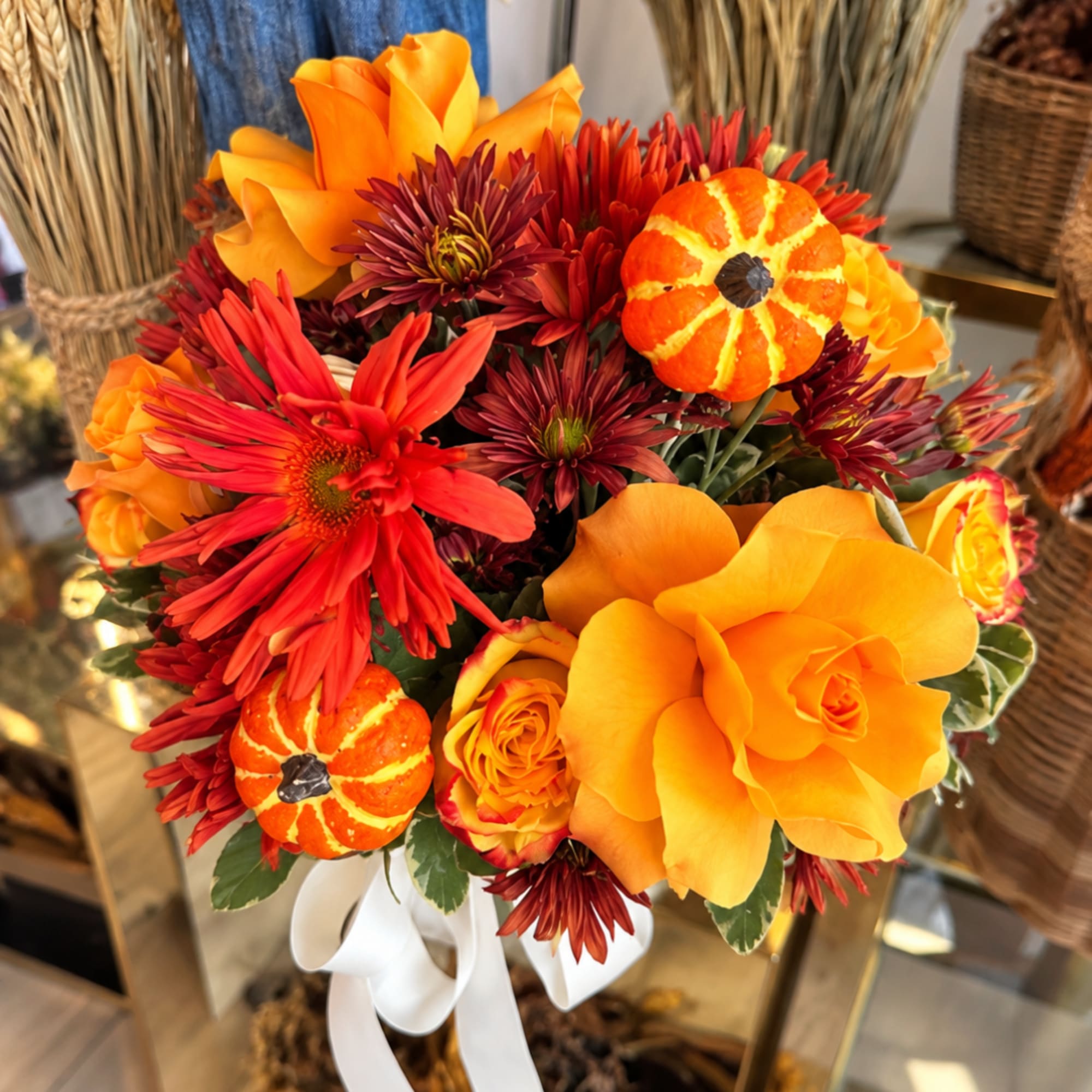 Orange and red floral bouquet with small pumpkin accents and a white ribbon
