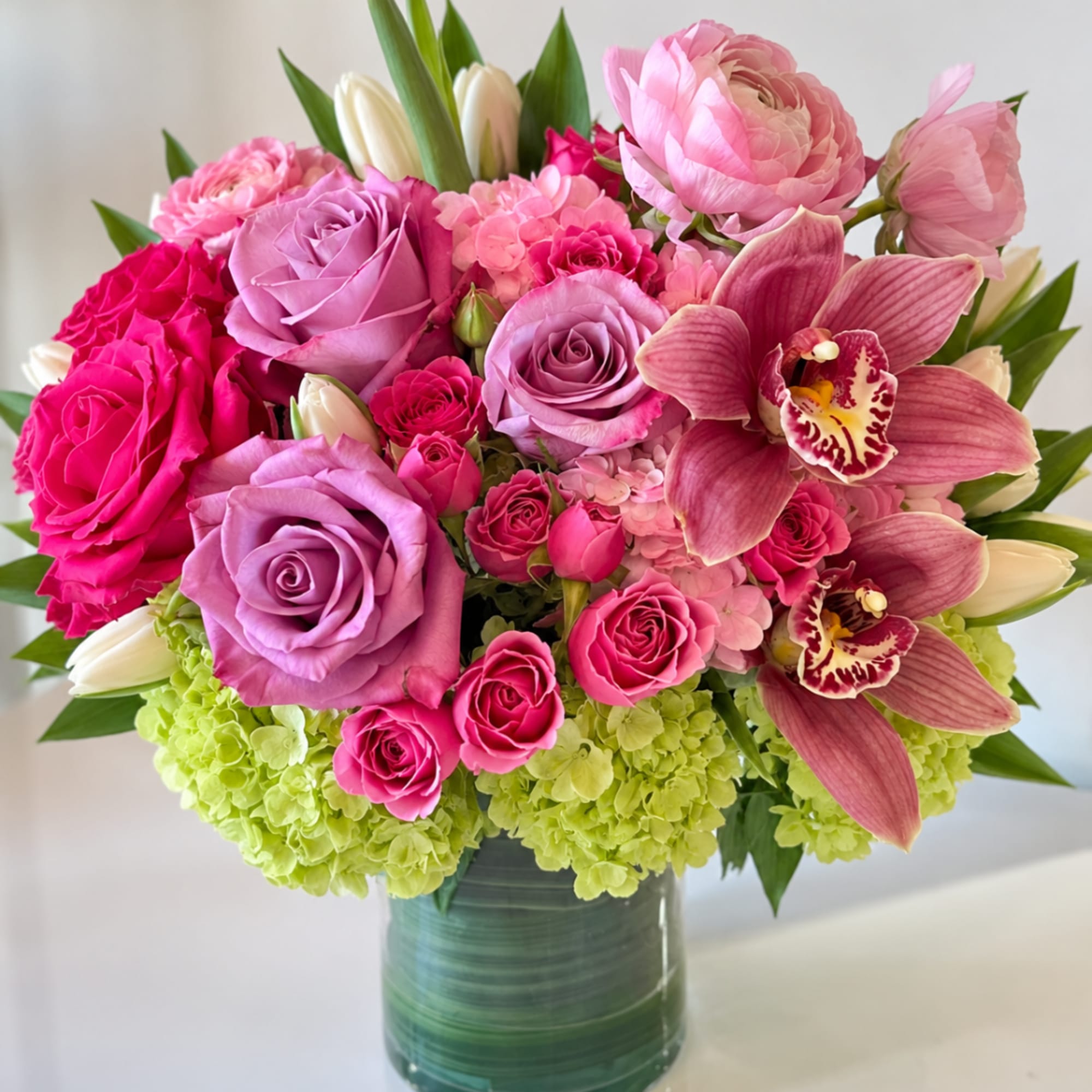 Pink and lavender roses with orchids in a glass vase