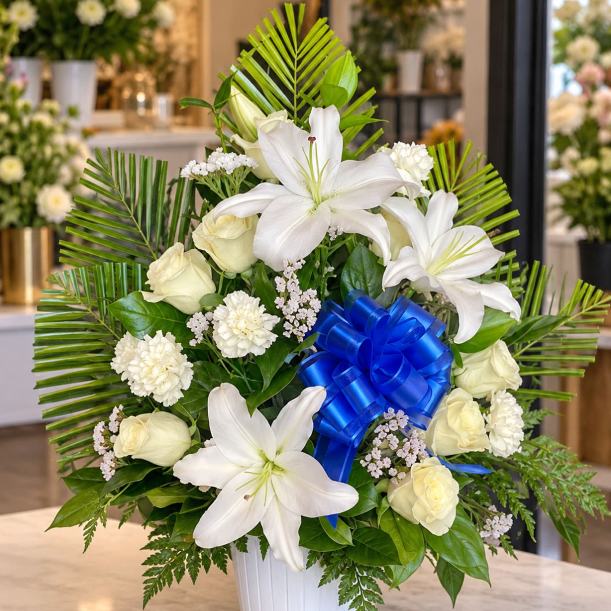 White lilies and roses arranged in a vase with a blue ribbon bow