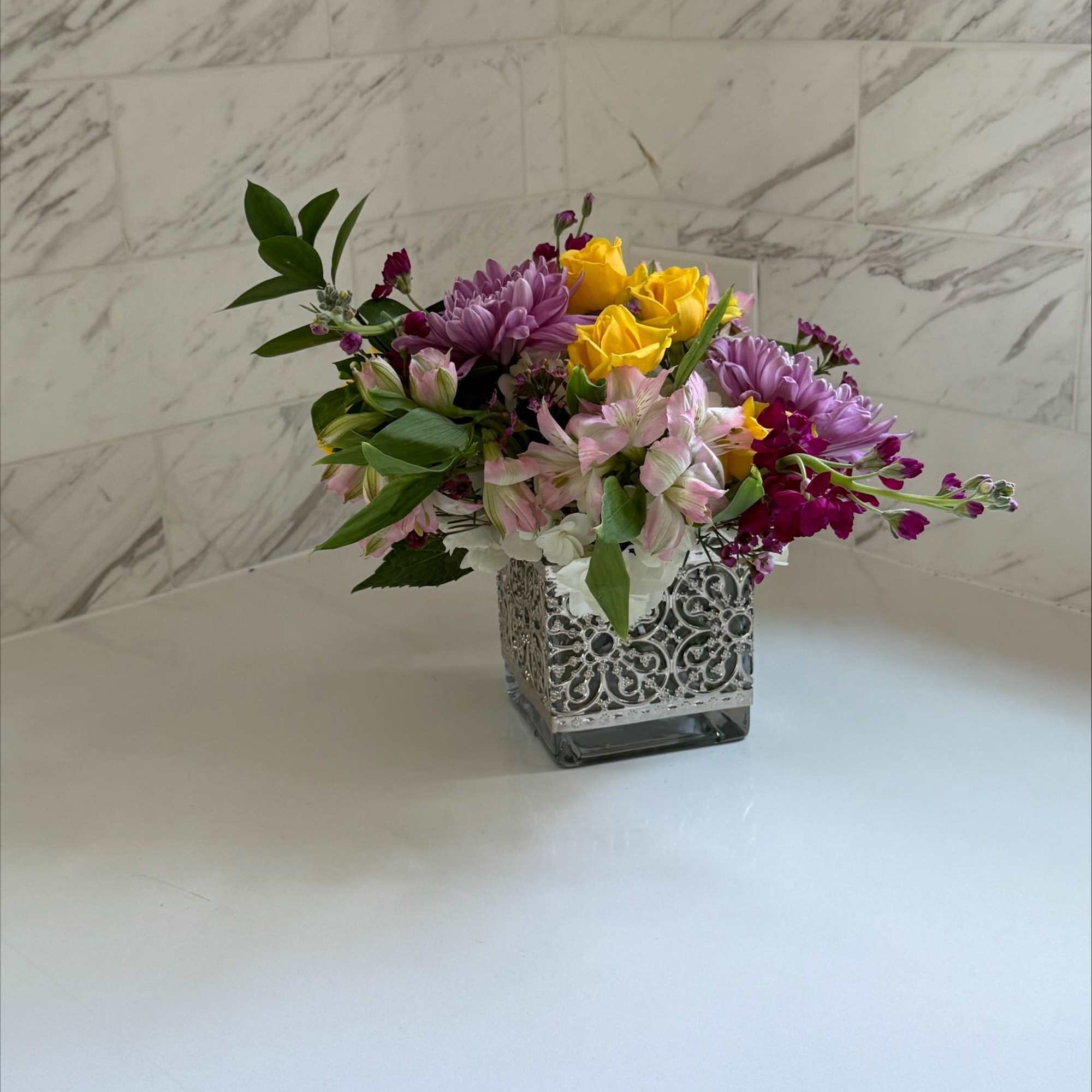 Mixed bouquet in a decorative square vase with yellow, purple, and pink flowers