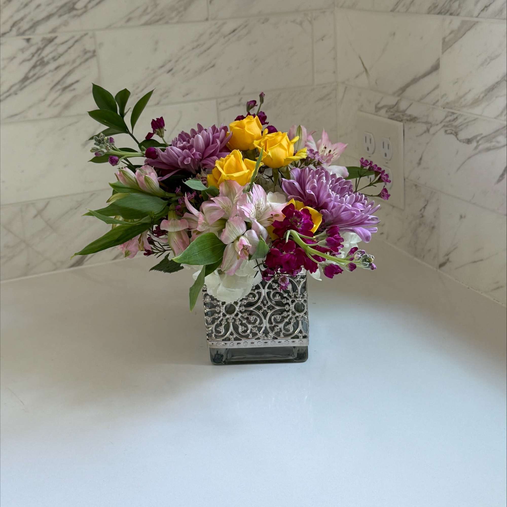 Mixed bouquet of yellow roses, purple mums, and pink alstroemeria in a decorative vase