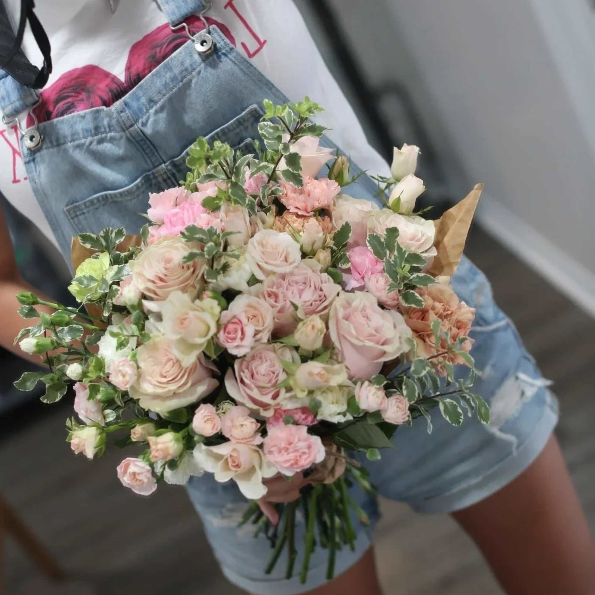 Handheld bouquet of pale pink and white roses with greenery