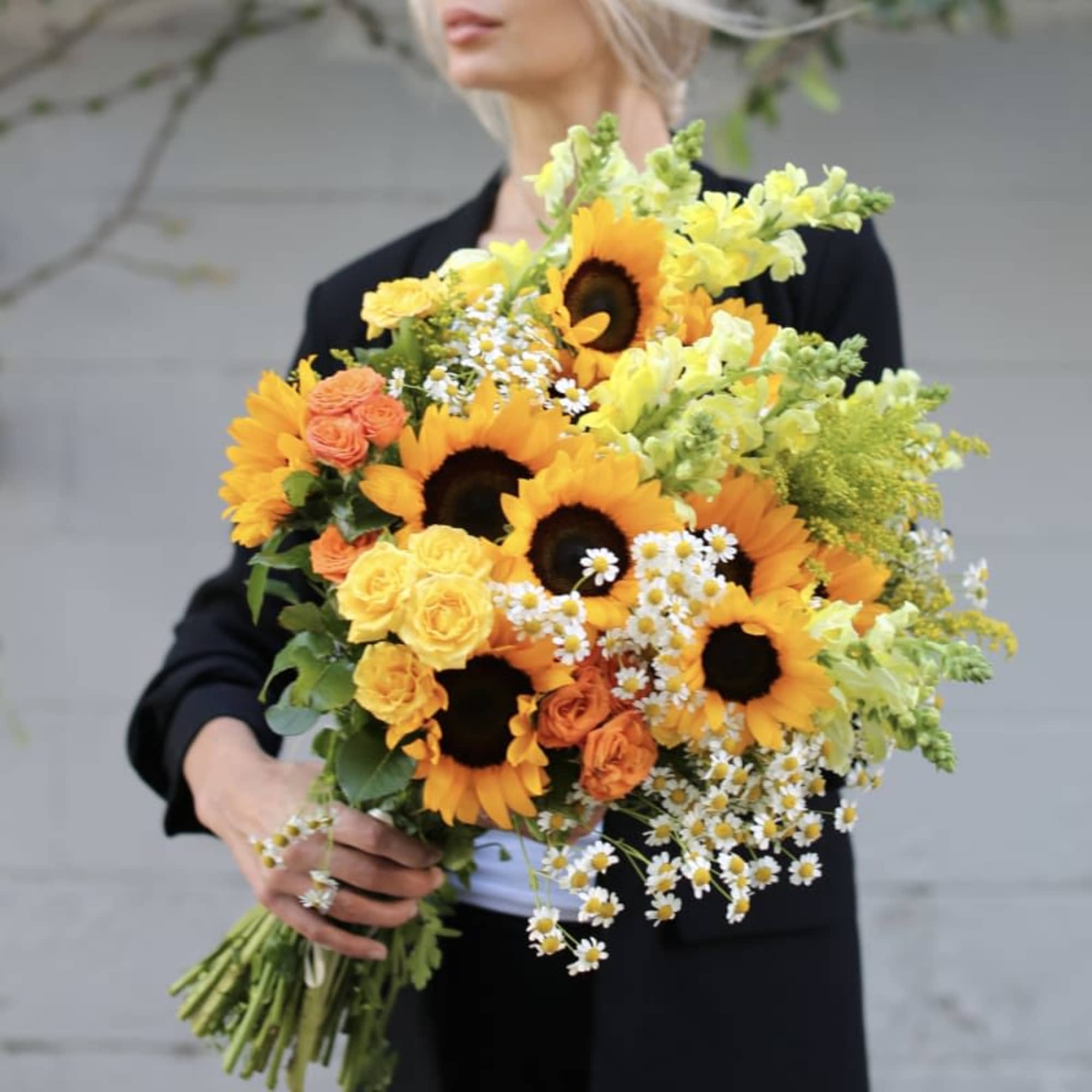 Woman holding a bouquet of sunflowers, roses, and small white daisies