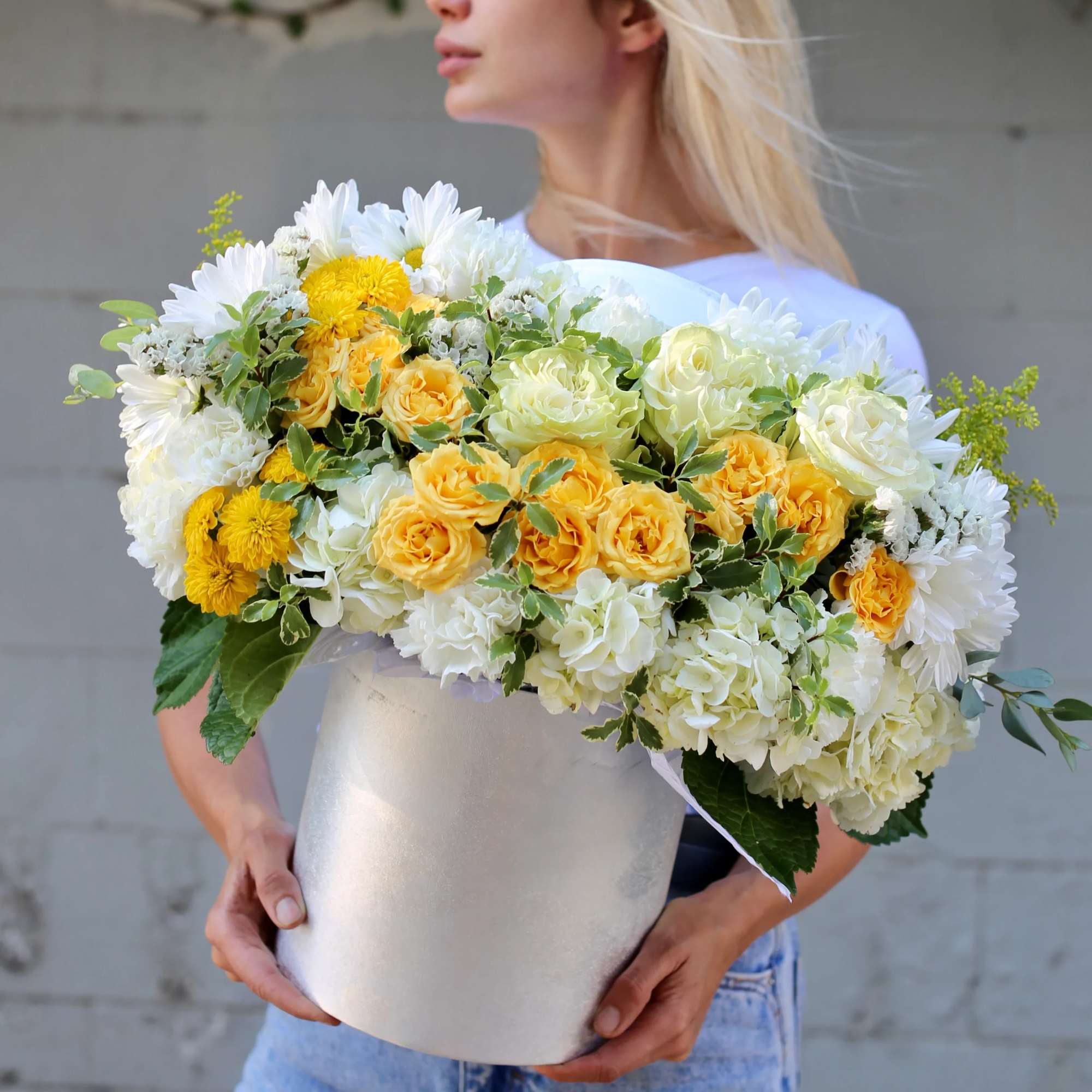 Woman holding a large bouquet of yellow and white flowers in a white box