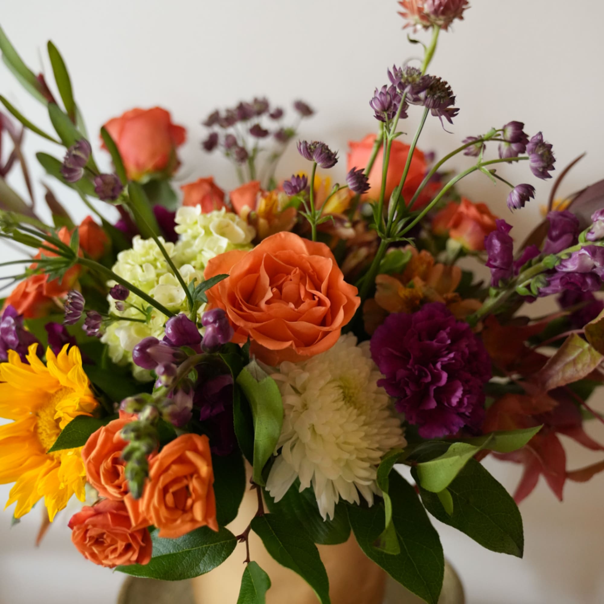 Mixed bouquet with orange roses, purple blooms, and white flowers in a vase