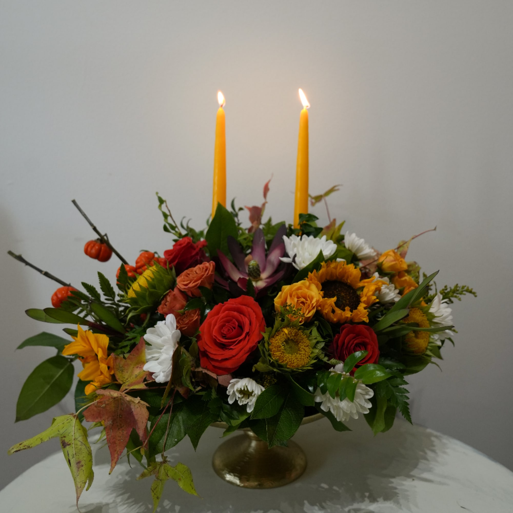Mixed floral centerpiece with two lit yellow candles in a gold pedestal vase
