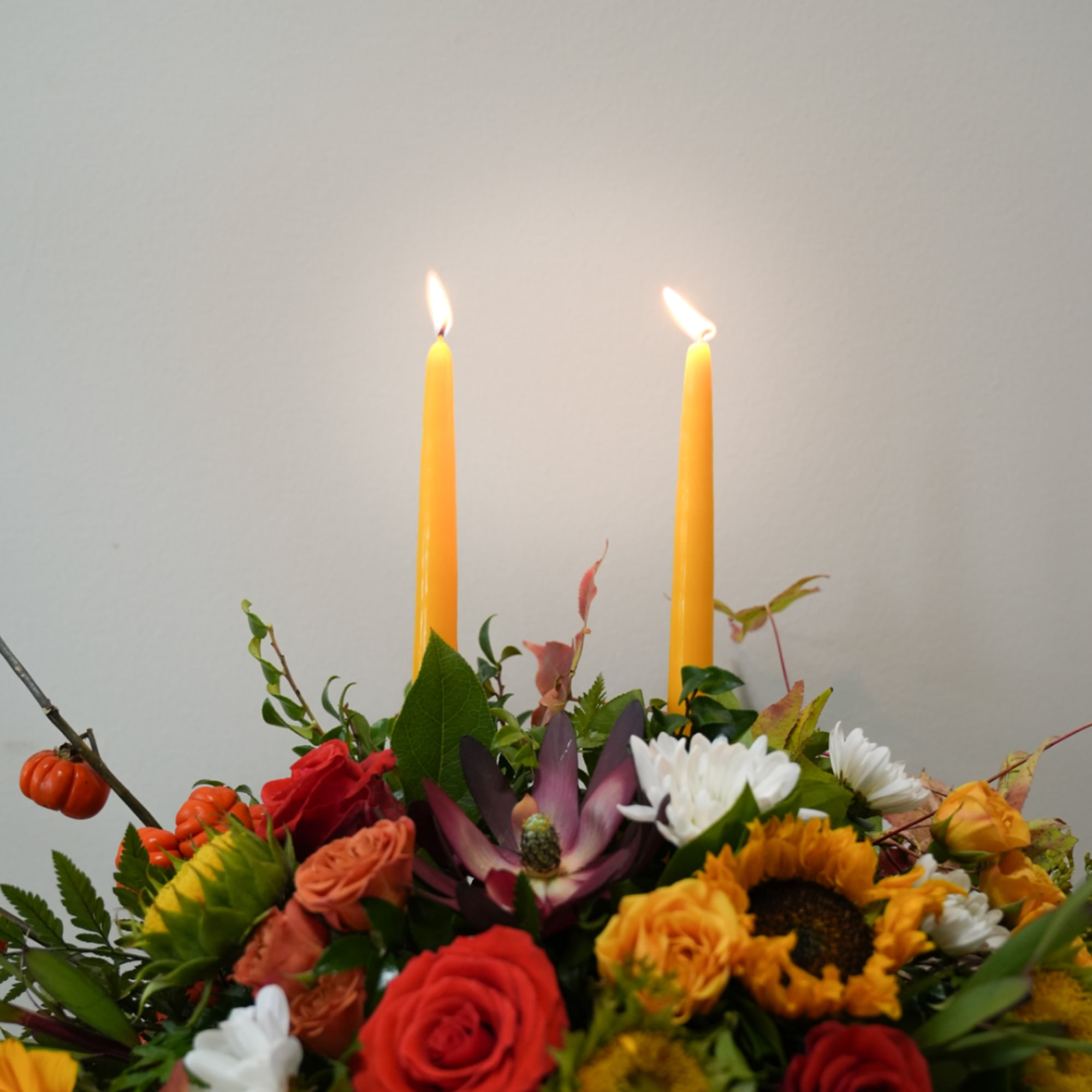 Floral arrangement with lit yellow taper candles and mixed blooms in autumn colors