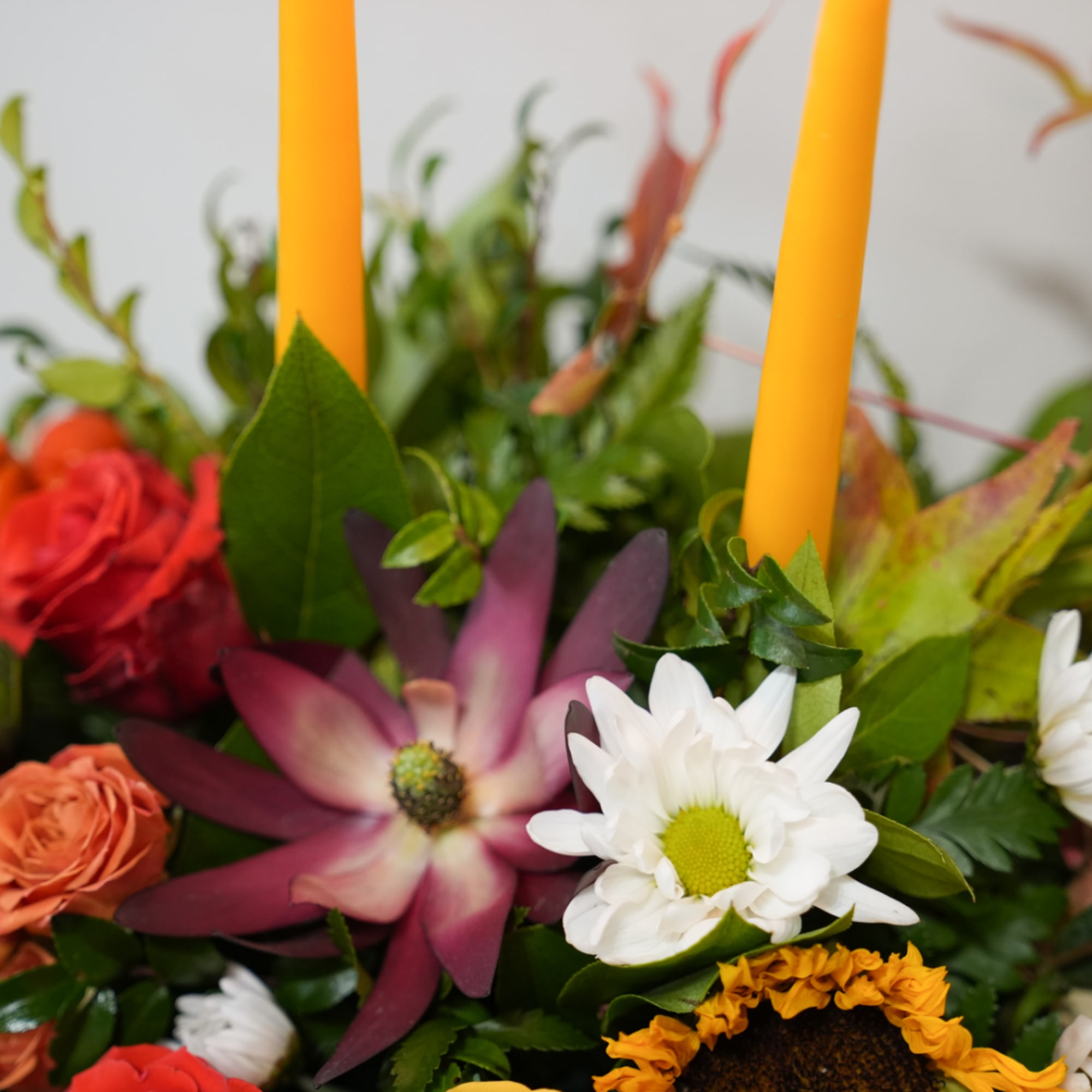 Mixed bouquet with red, peach, and white flowers and two yellow taper candles