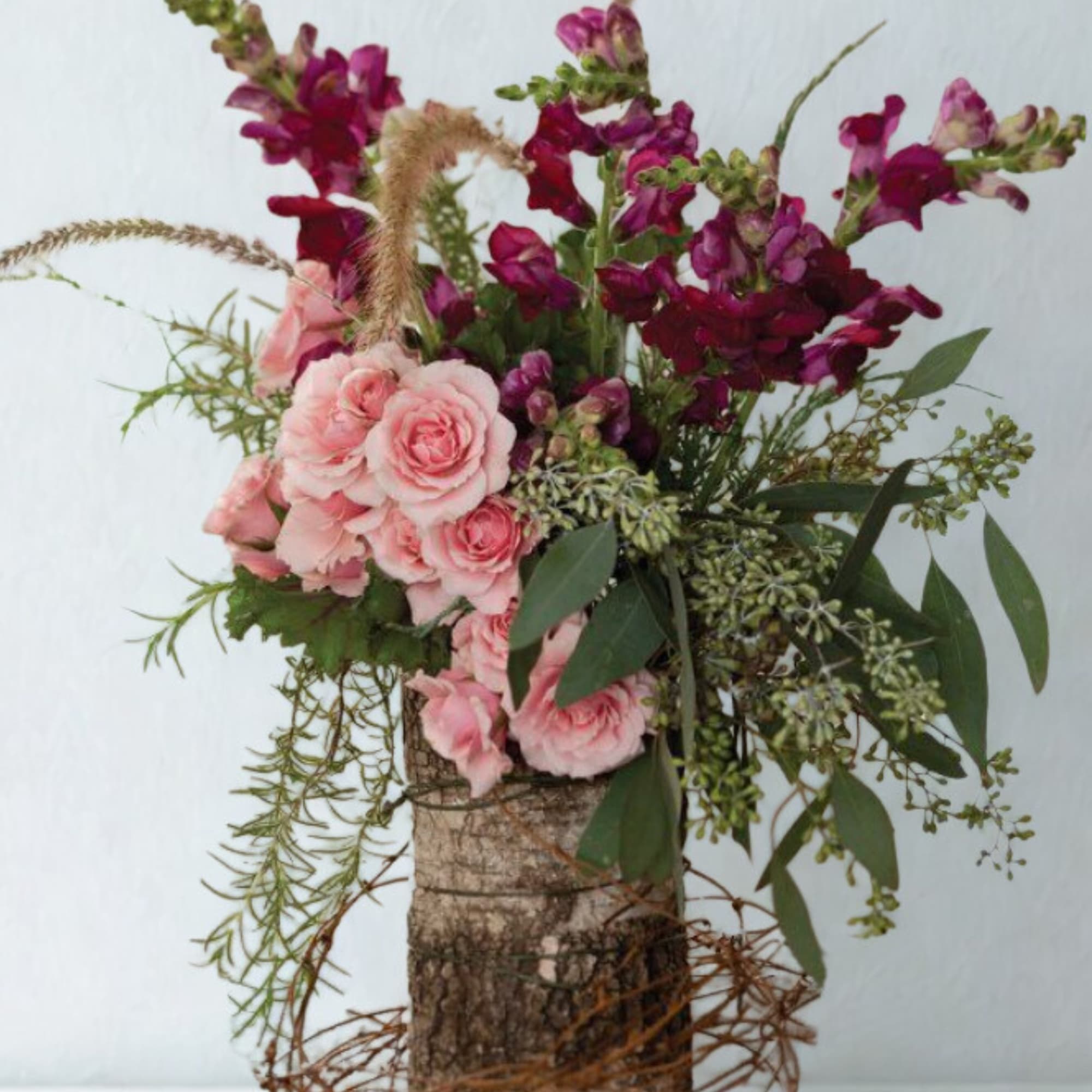 Pink roses and magenta snapdragons in a rustic bark container