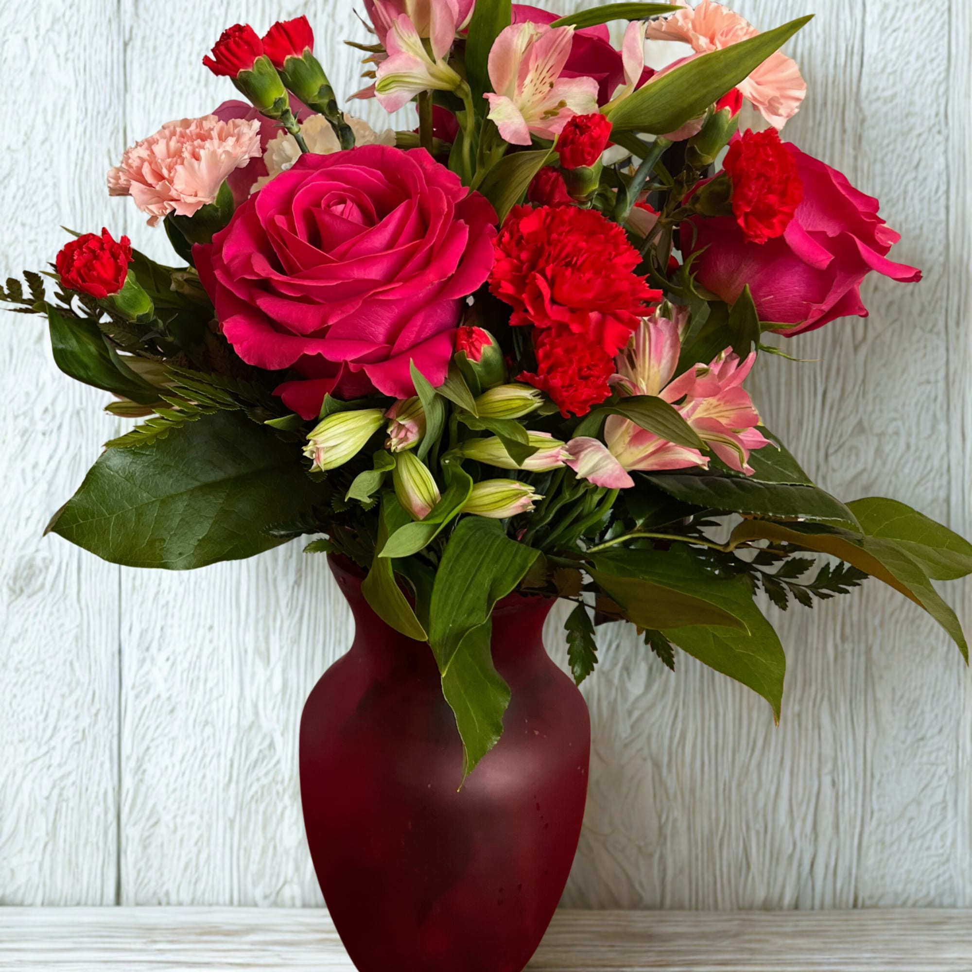 Pink roses and red carnations arranged in a burgundy vase