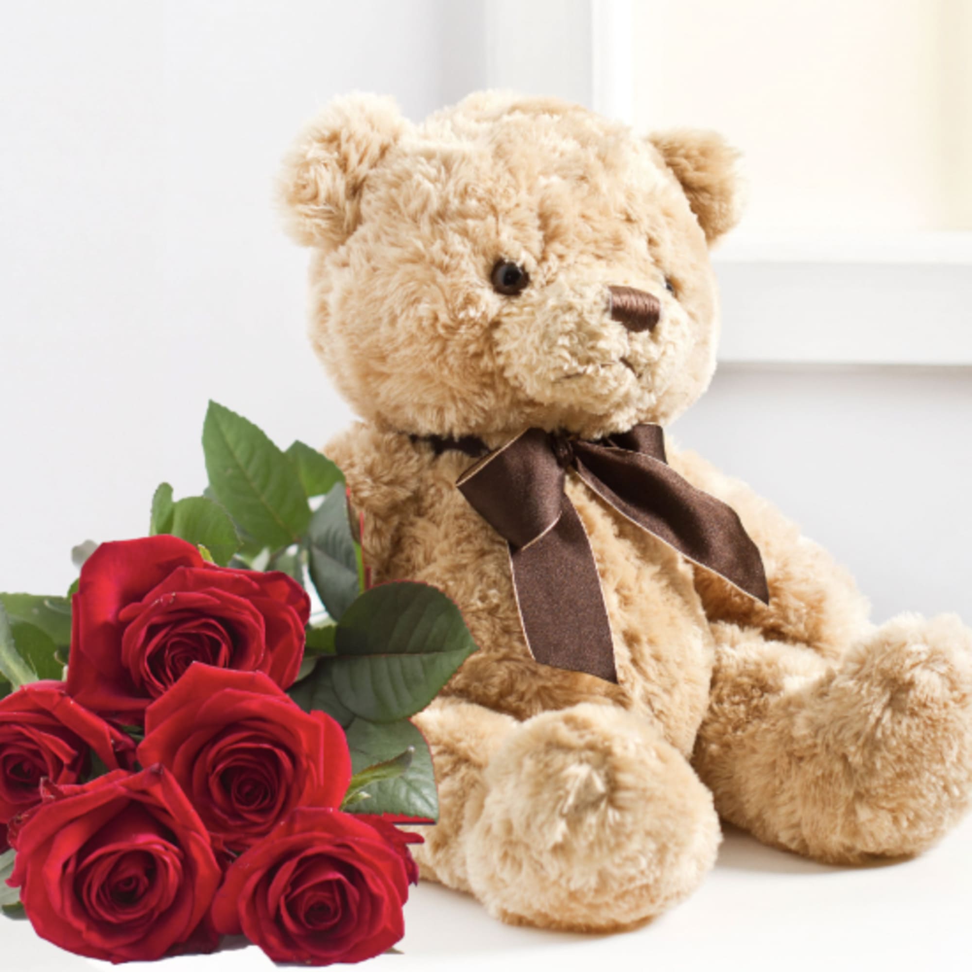 Red roses beside a tan teddy bear with a brown ribbon
