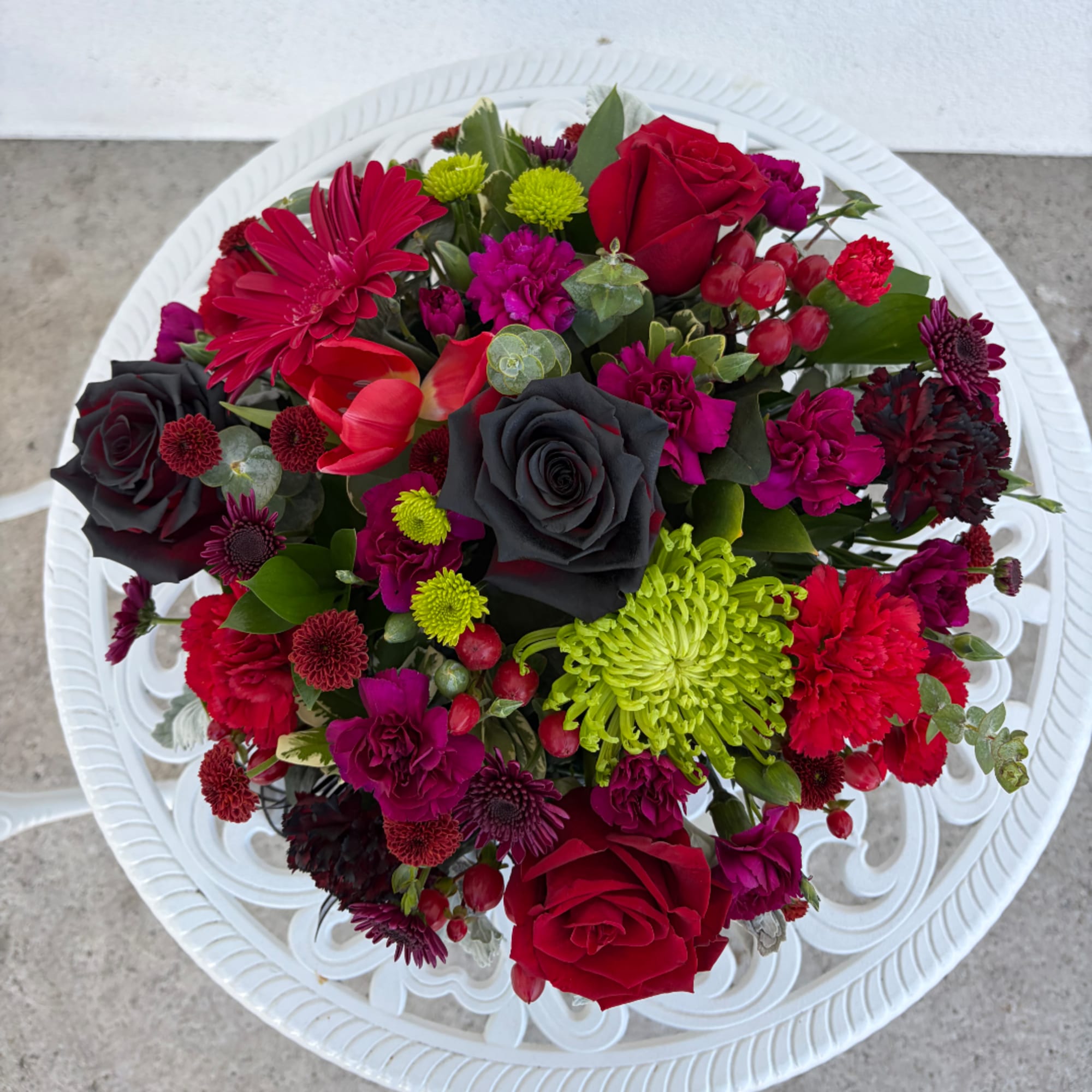 Mixed bouquet of red, black, and magenta flowers on a white tray