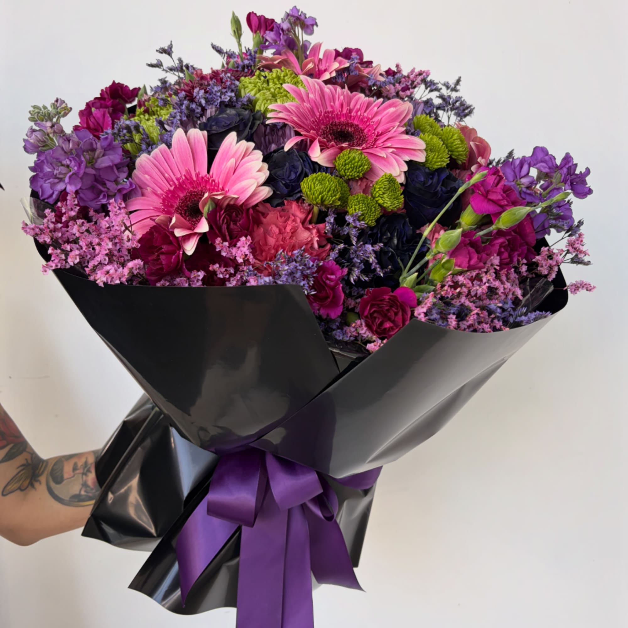 Bouquet of pink and purple flowers wrapped in black paper with a purple ribbon