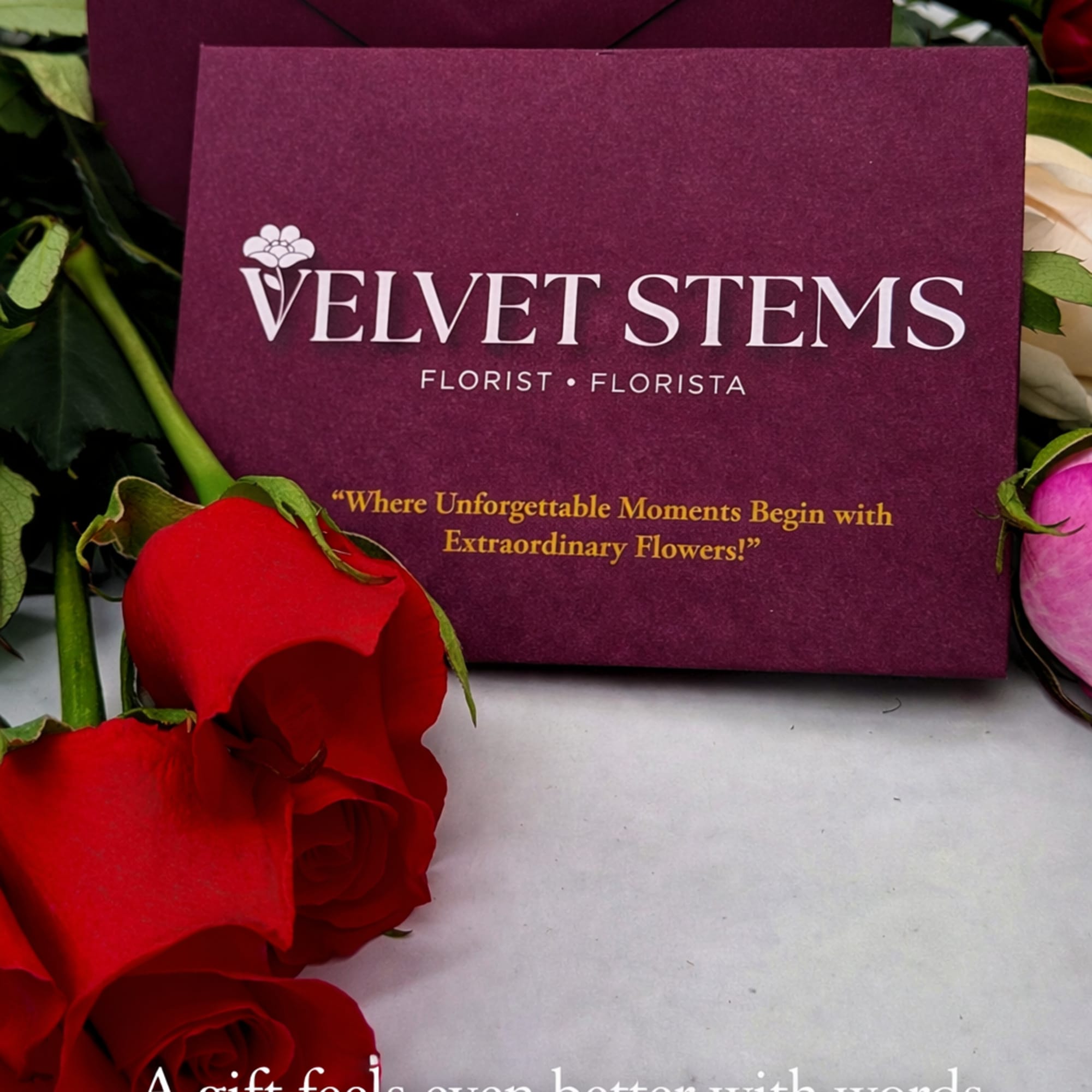 Branded burgundy stationery card and envelope surrounded by red, white, and pink roses.