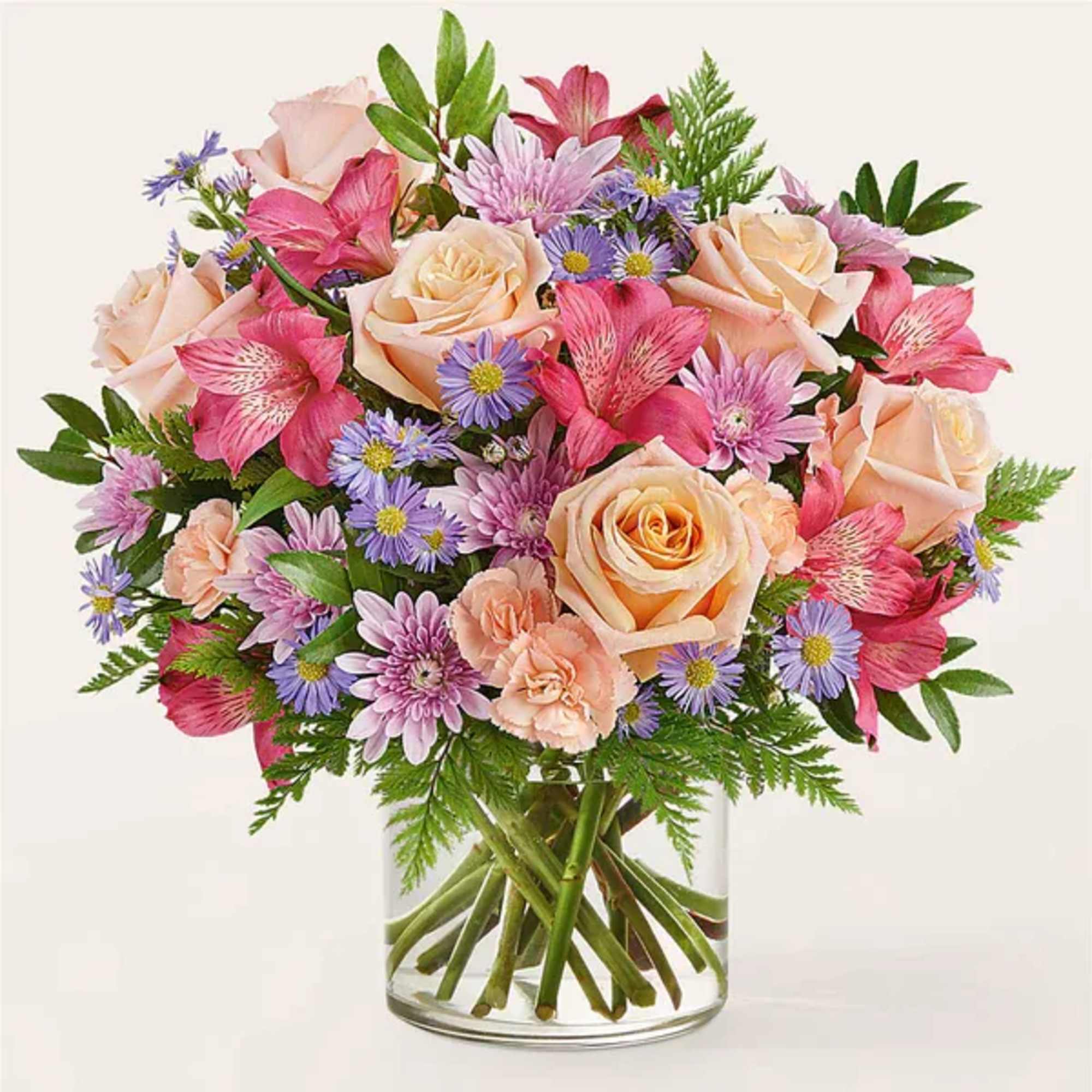 Mixed bouquet of peach roses, pink alstroemeria, and purple daisies in a glass vase