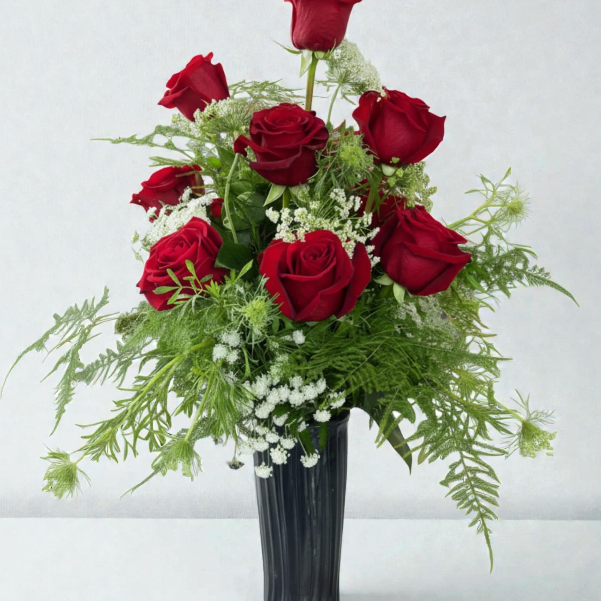 Red roses arranged in a black vase with airy white filler flowers