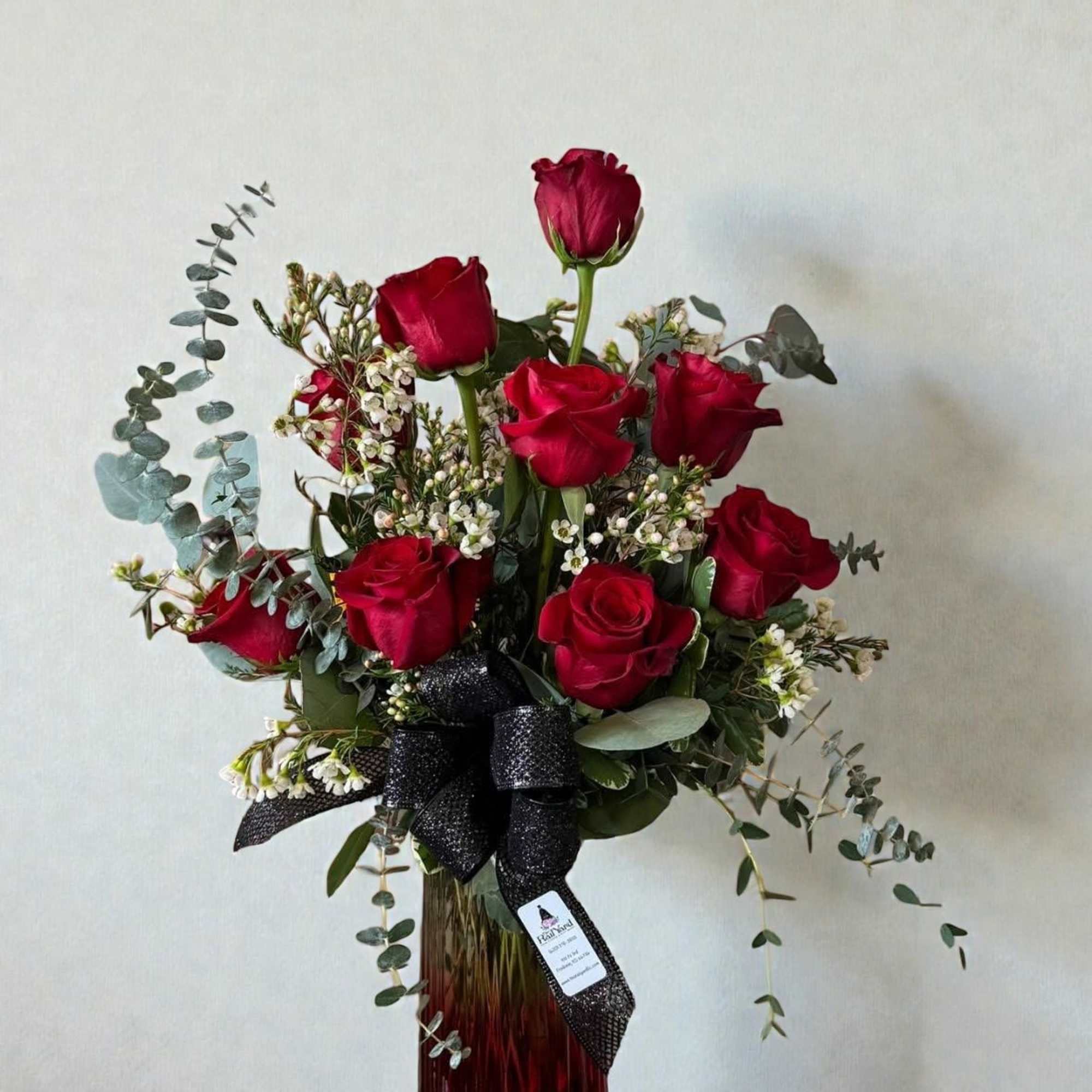 Red roses in a tall glass vase with white filler flowers and eucalyptus