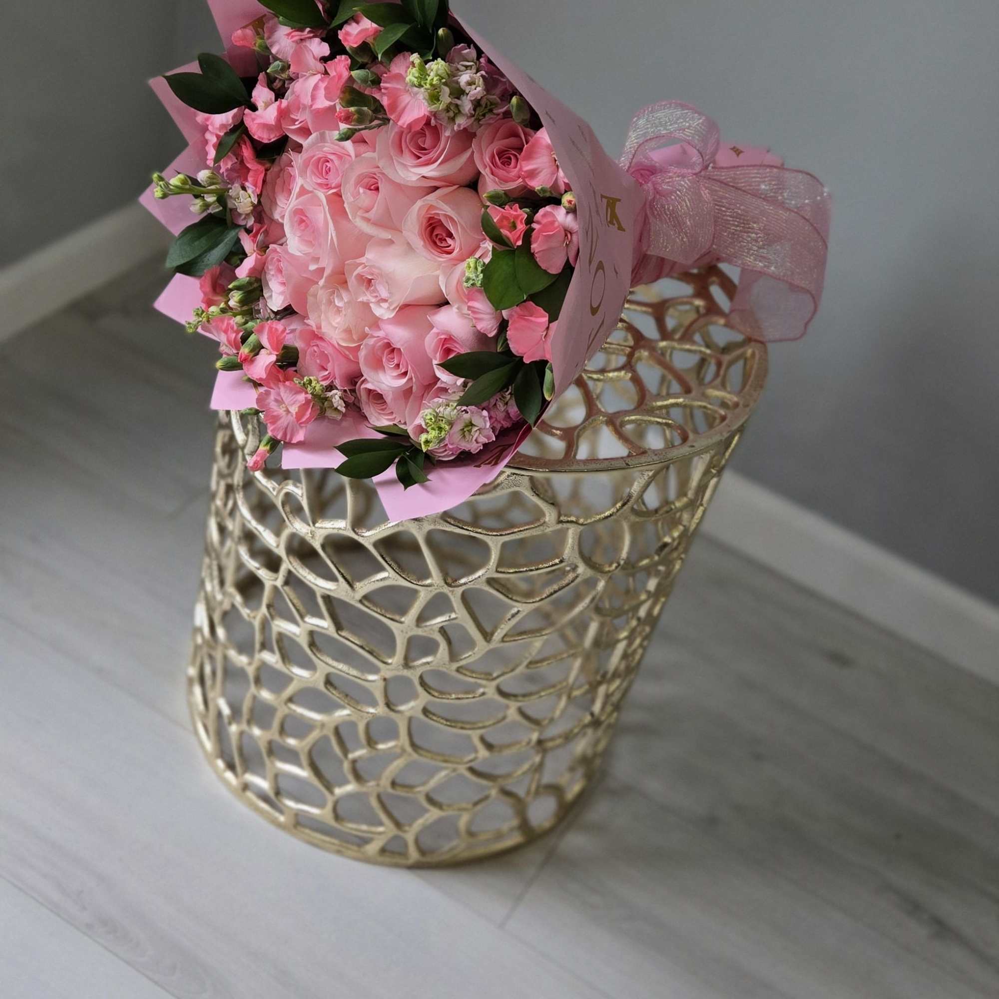 Pink rose bouquet wrapped in pink paper with a ribbon, resting on a gold decorative stand
