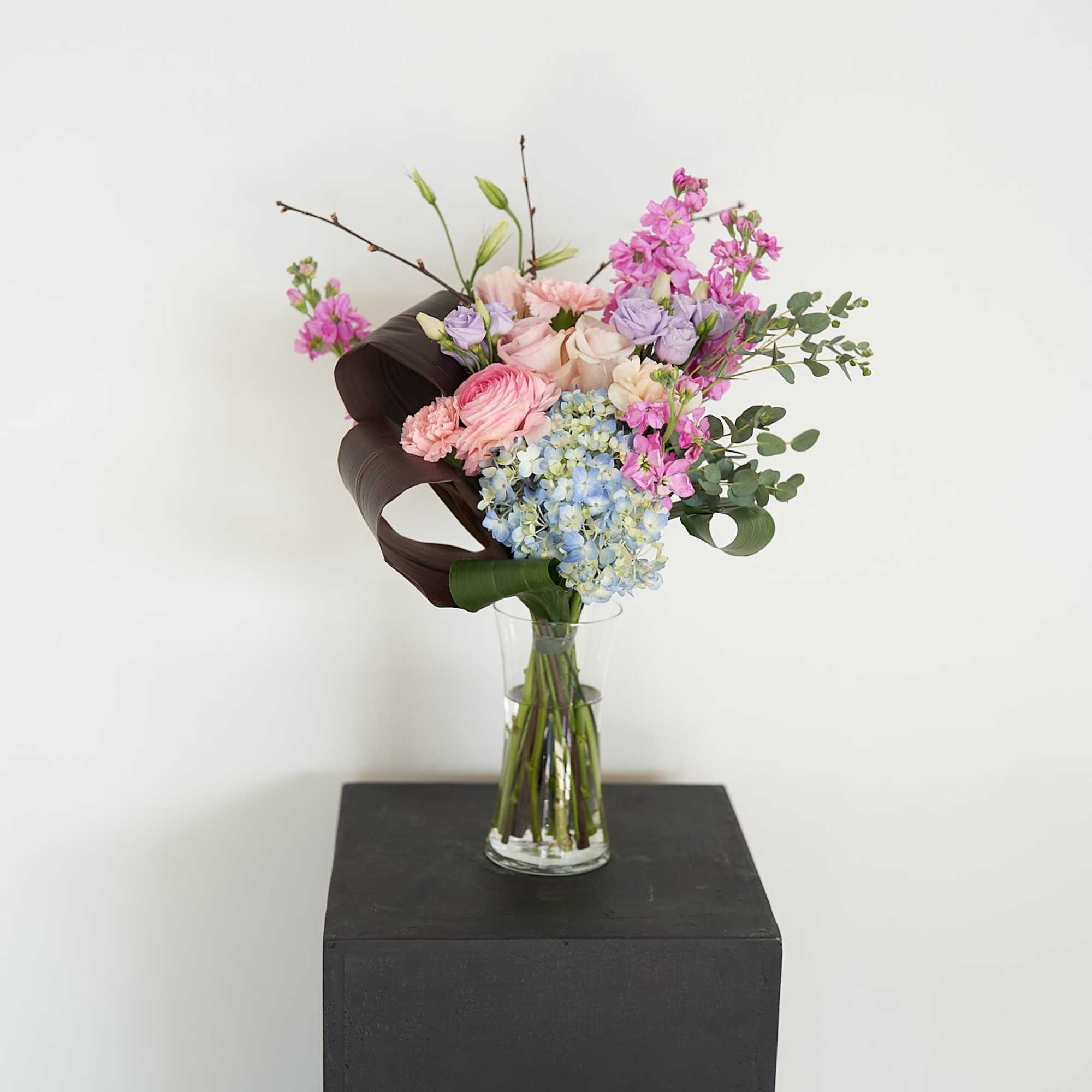 Mixed pastel bouquet in a clear glass vase on a black pedestal