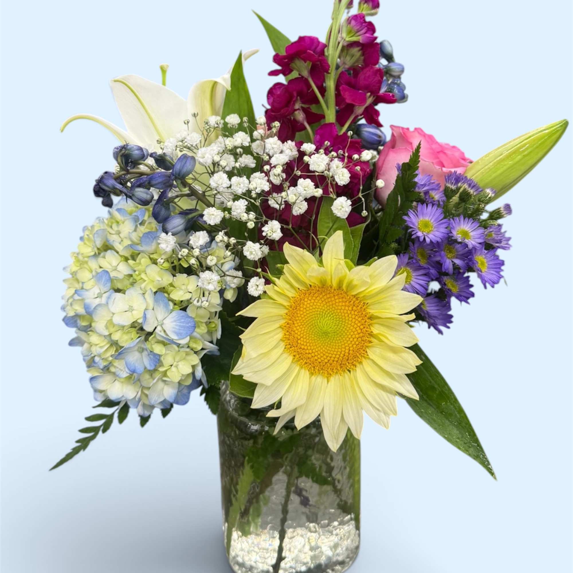 Mixed bouquet in a glass vase with a yellow sunflower, pink rose, and purple blooms