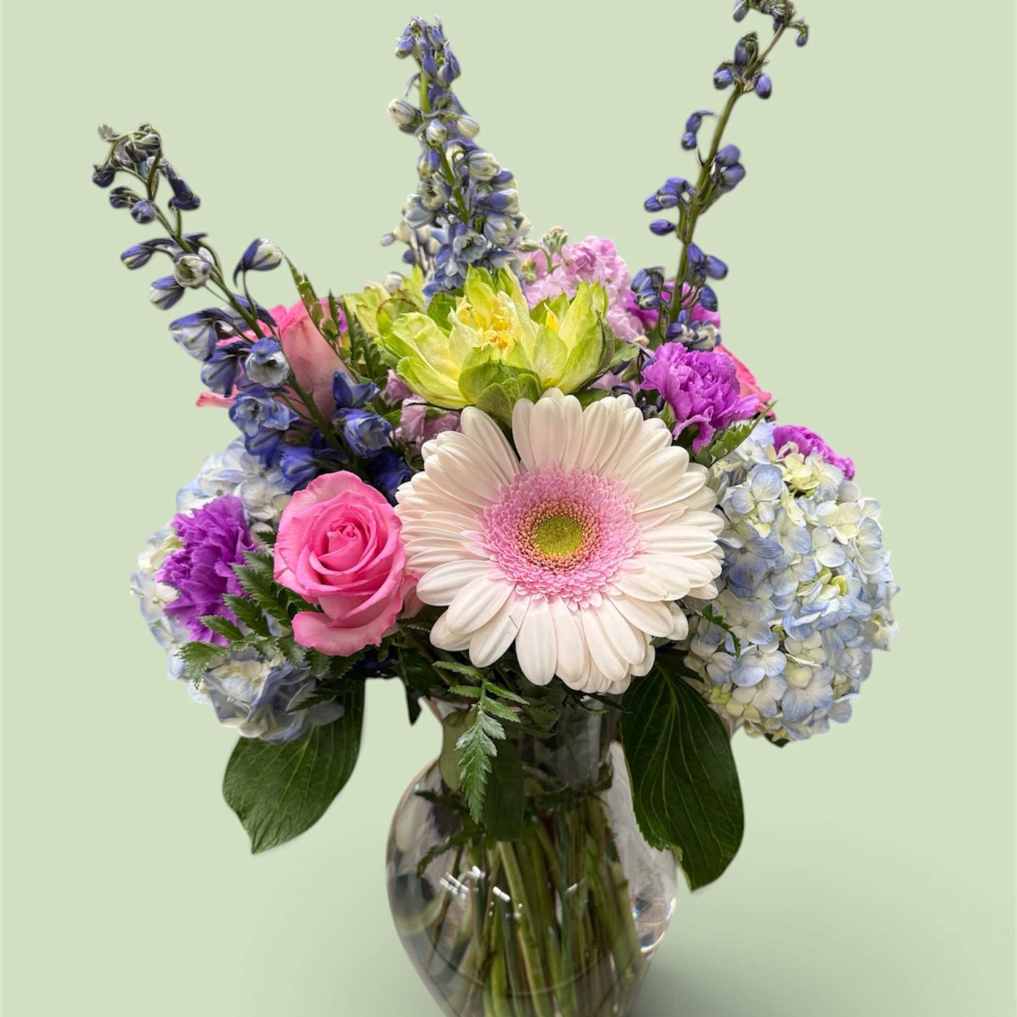 Mixed bouquet in a clear glass vase with a pink gerbera daisy and blue-purple blooms
