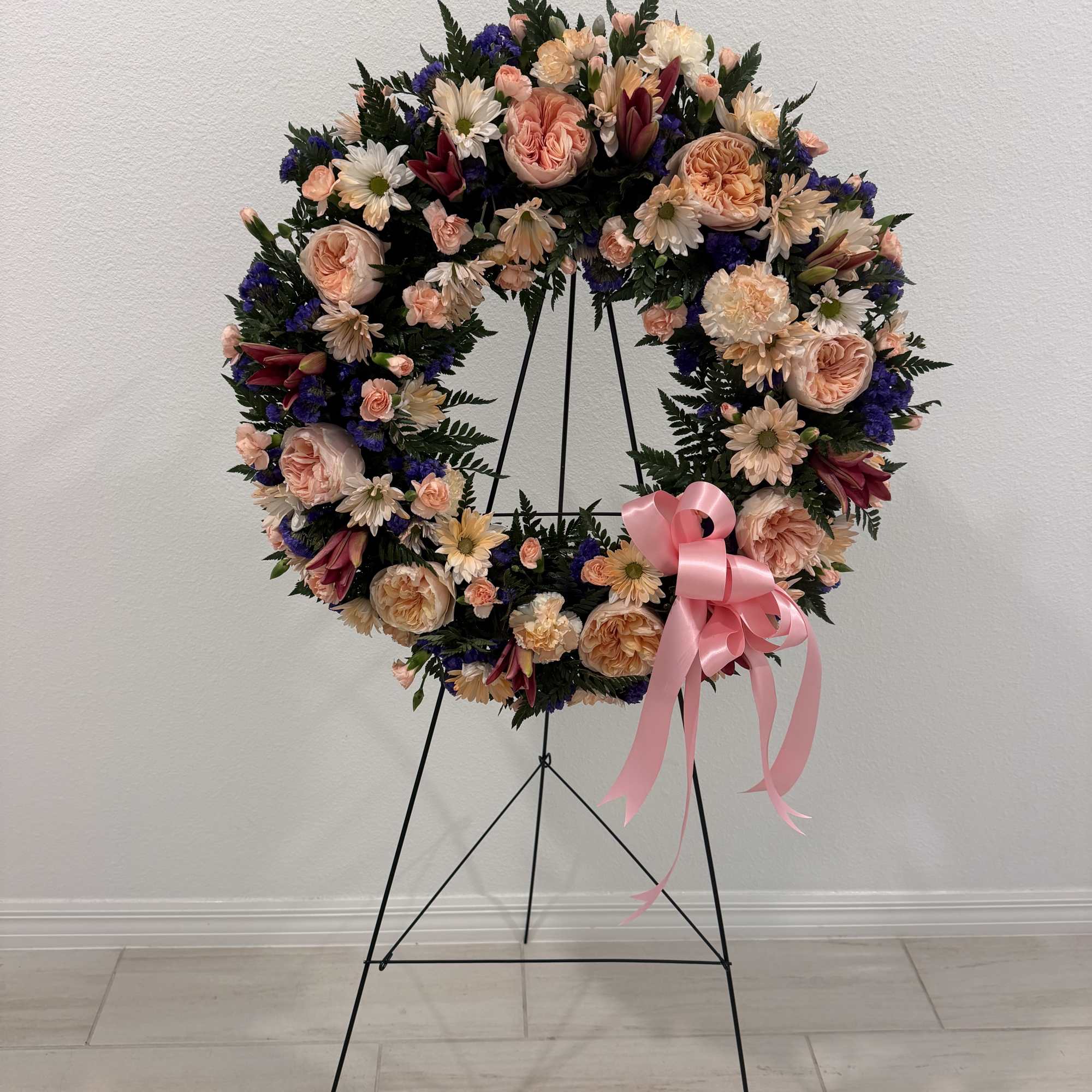 Large floral wreath on a black stand with a pink ribbon bow