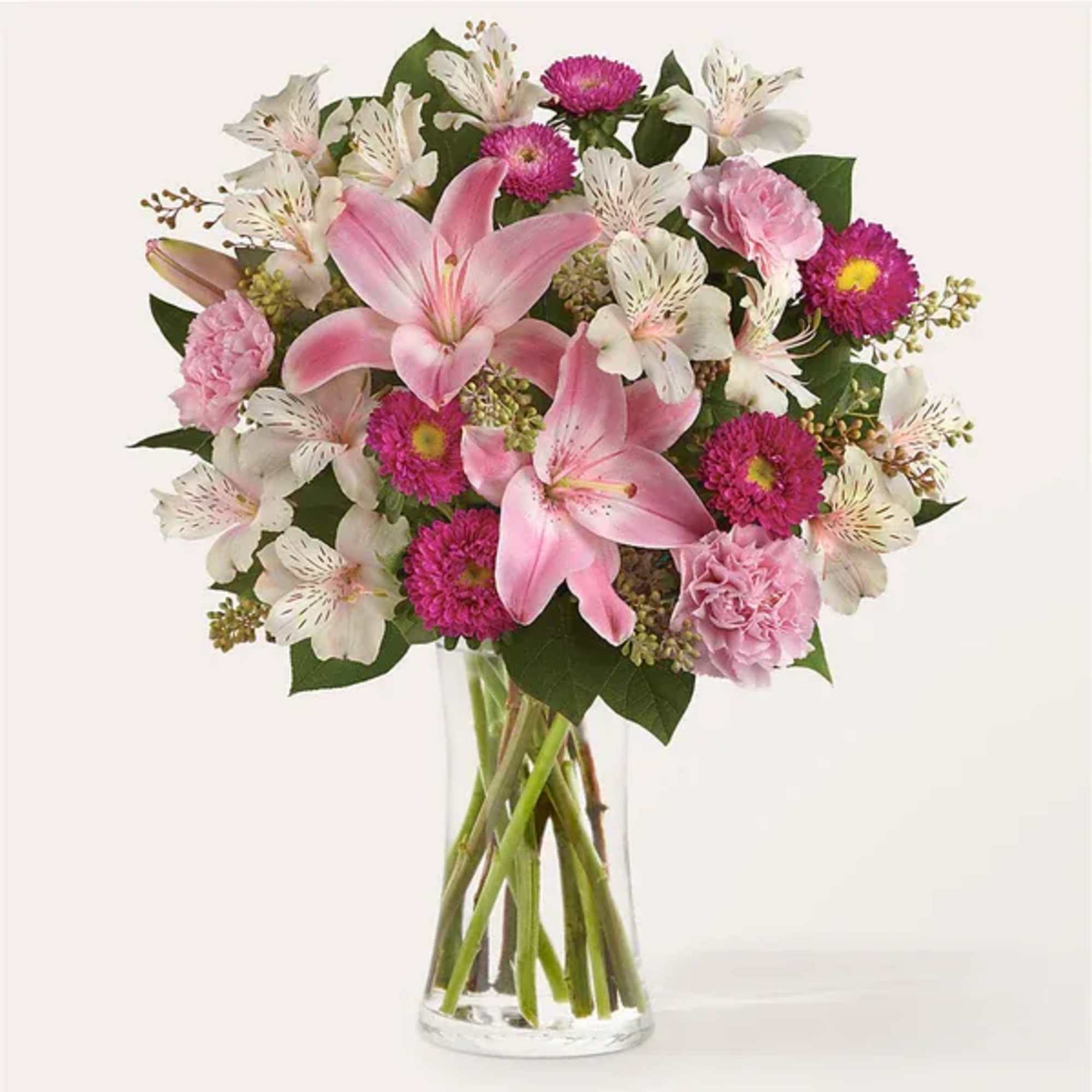 Pink lilies and mixed flowers arranged in a clear glass vase