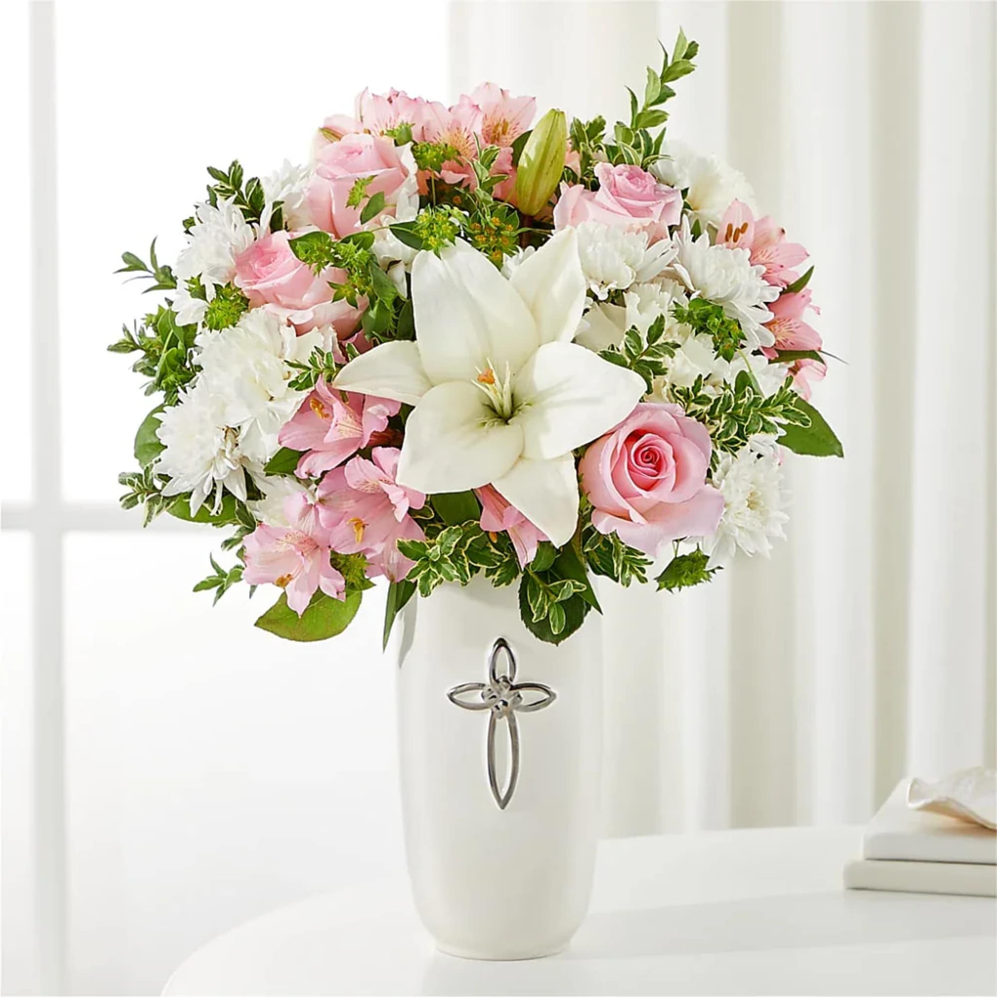 Pink and white flower arrangement in a white vase with a cross emblem