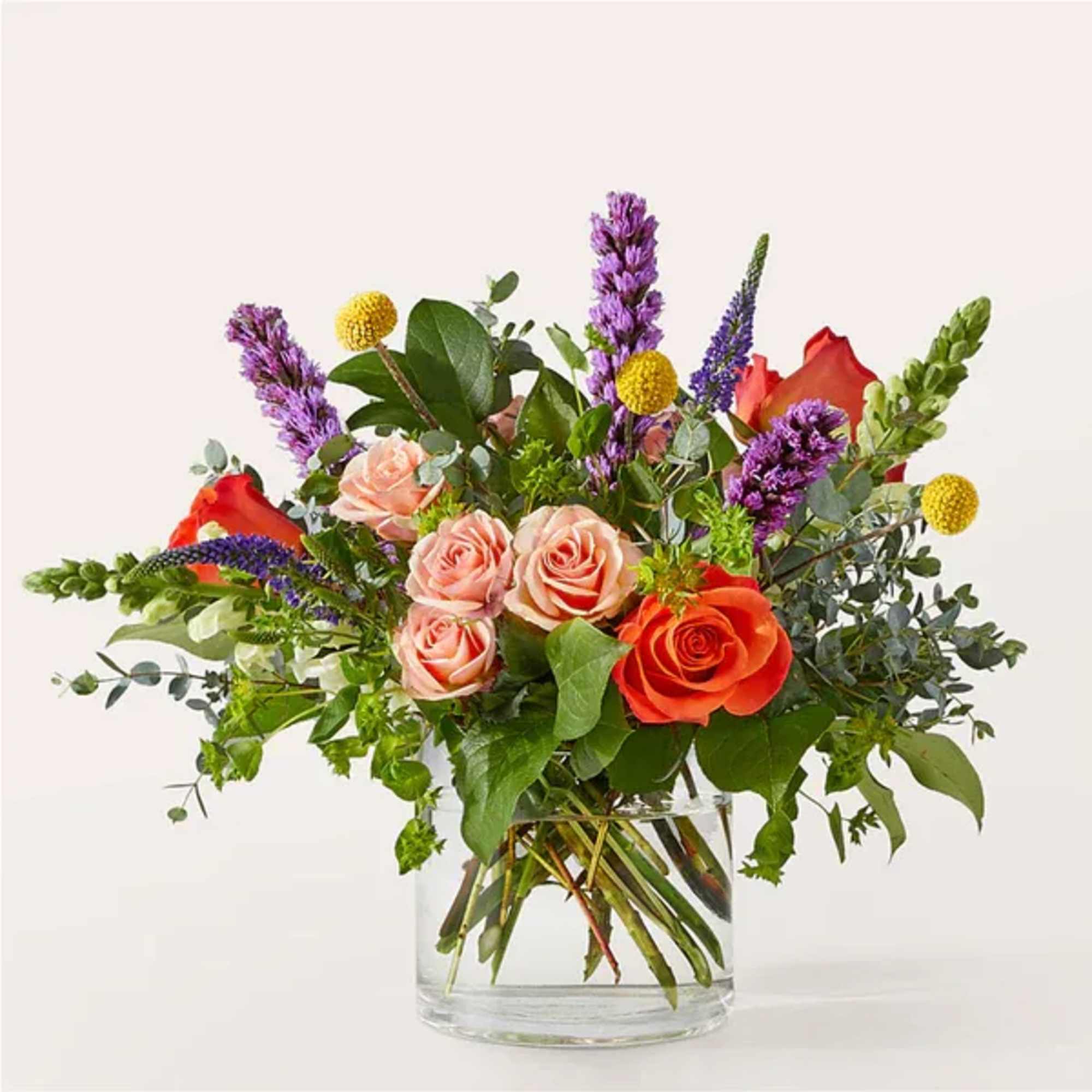 Mixed bouquet of roses and purple spikes in a clear glass vase
