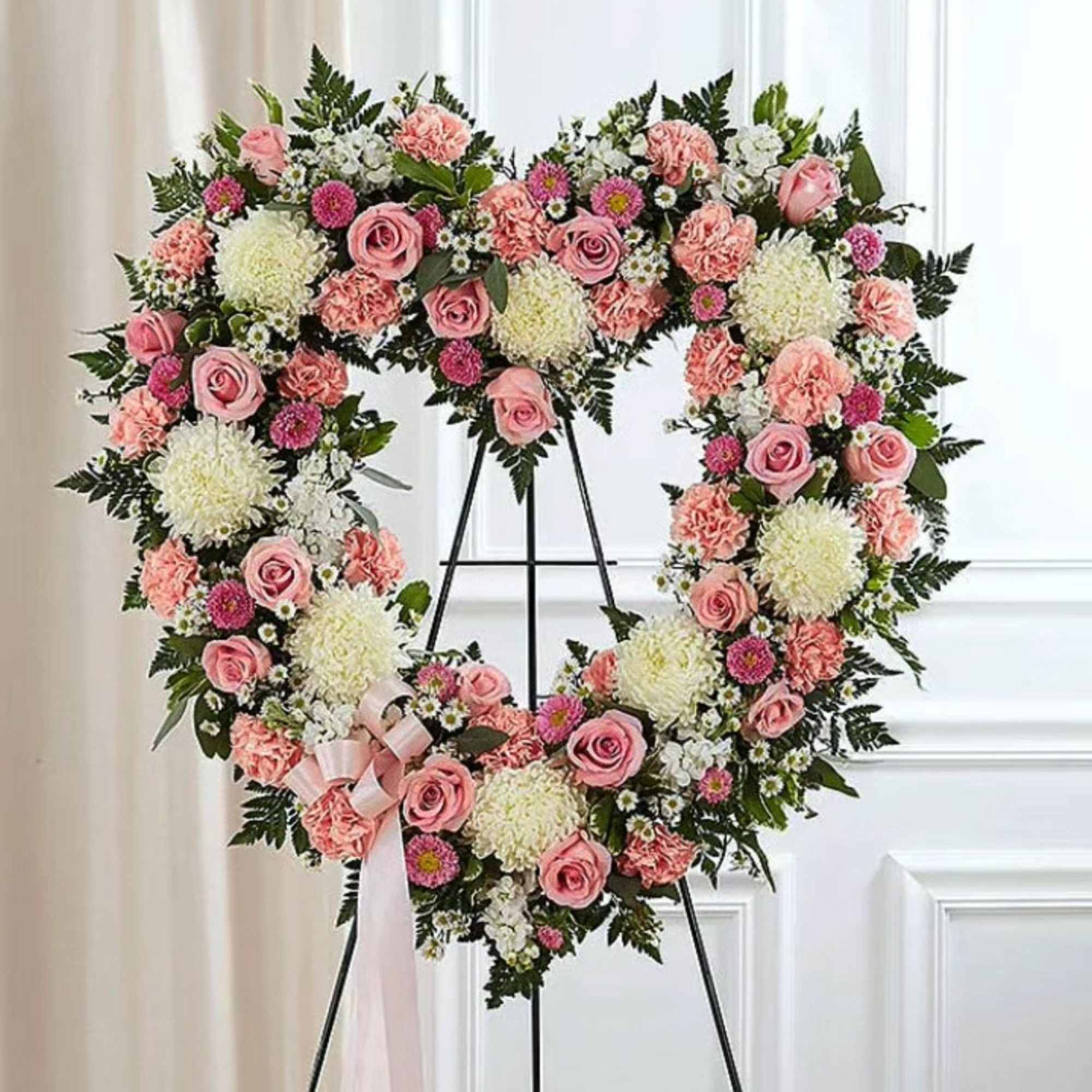 Heart-shaped floral wreath with pink roses and white blooms on a stand