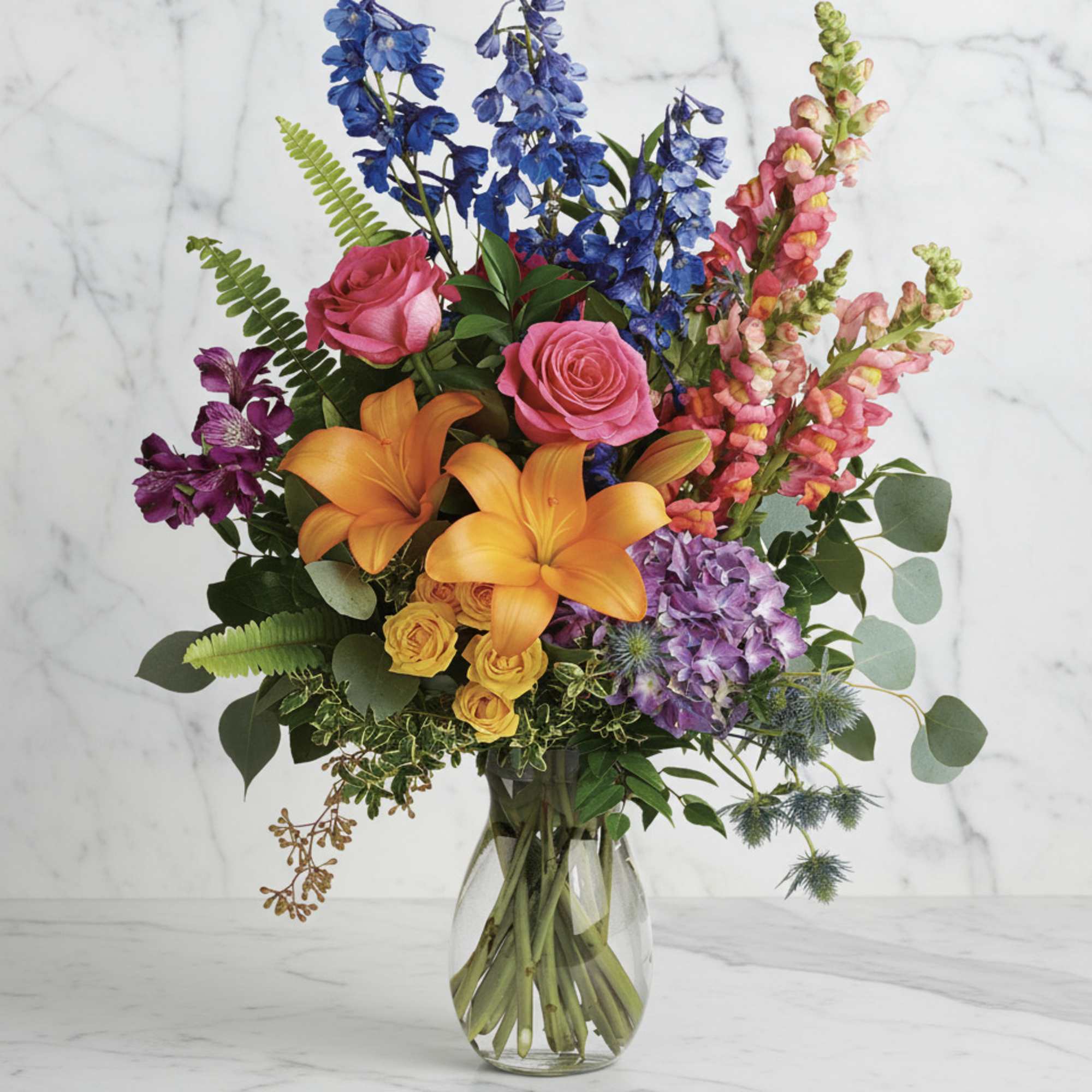Colorful bouquet with roses, lilies, delphinium, and snapdragons in a glass vase