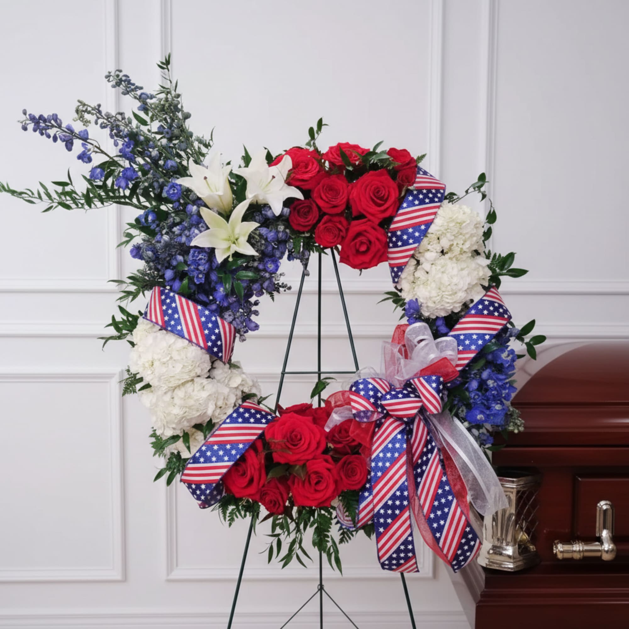 Red, white, and blue floral wreath on a stand with ribbon bows
