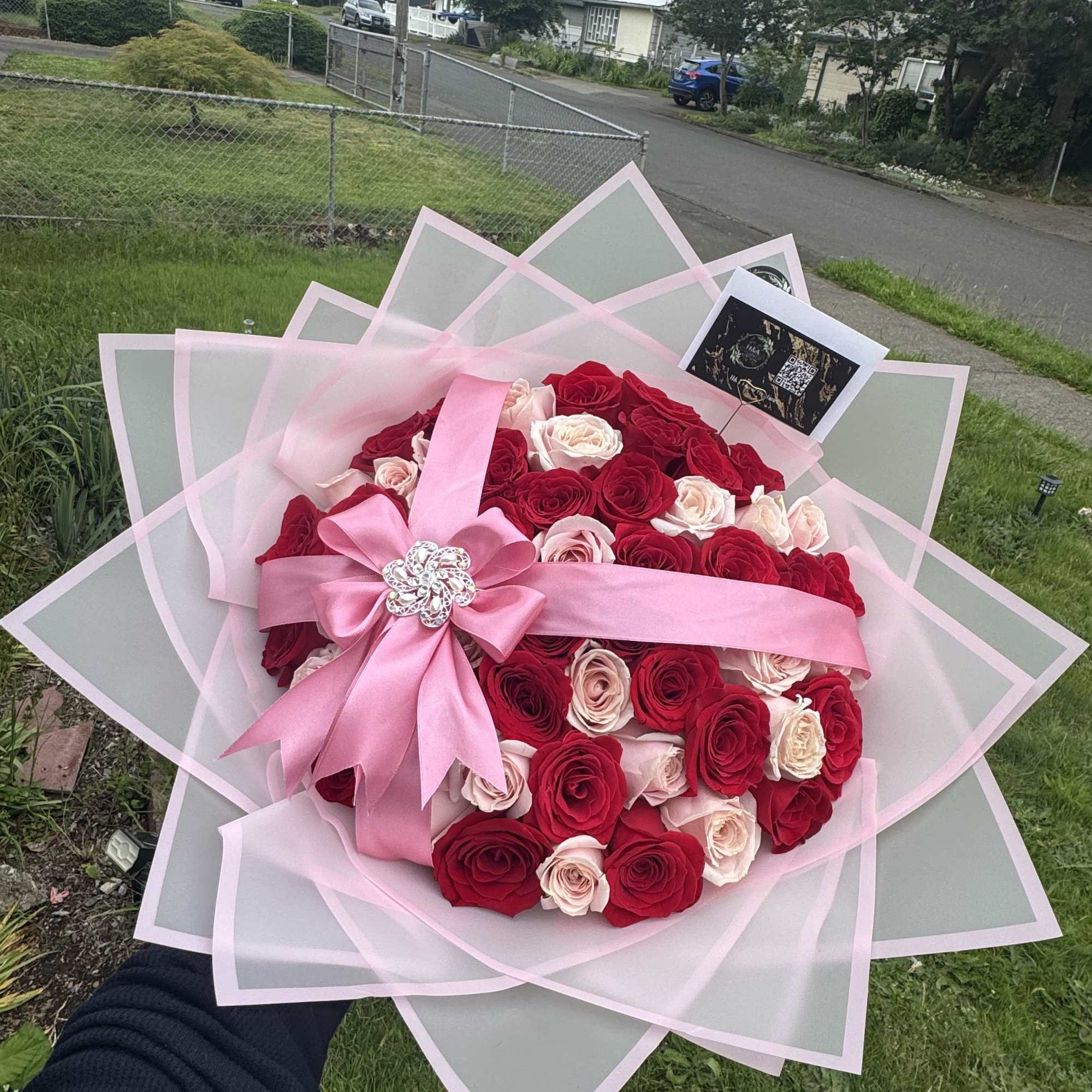 Large bouquet of red and blush roses wrapped in pink paper with a ribbon