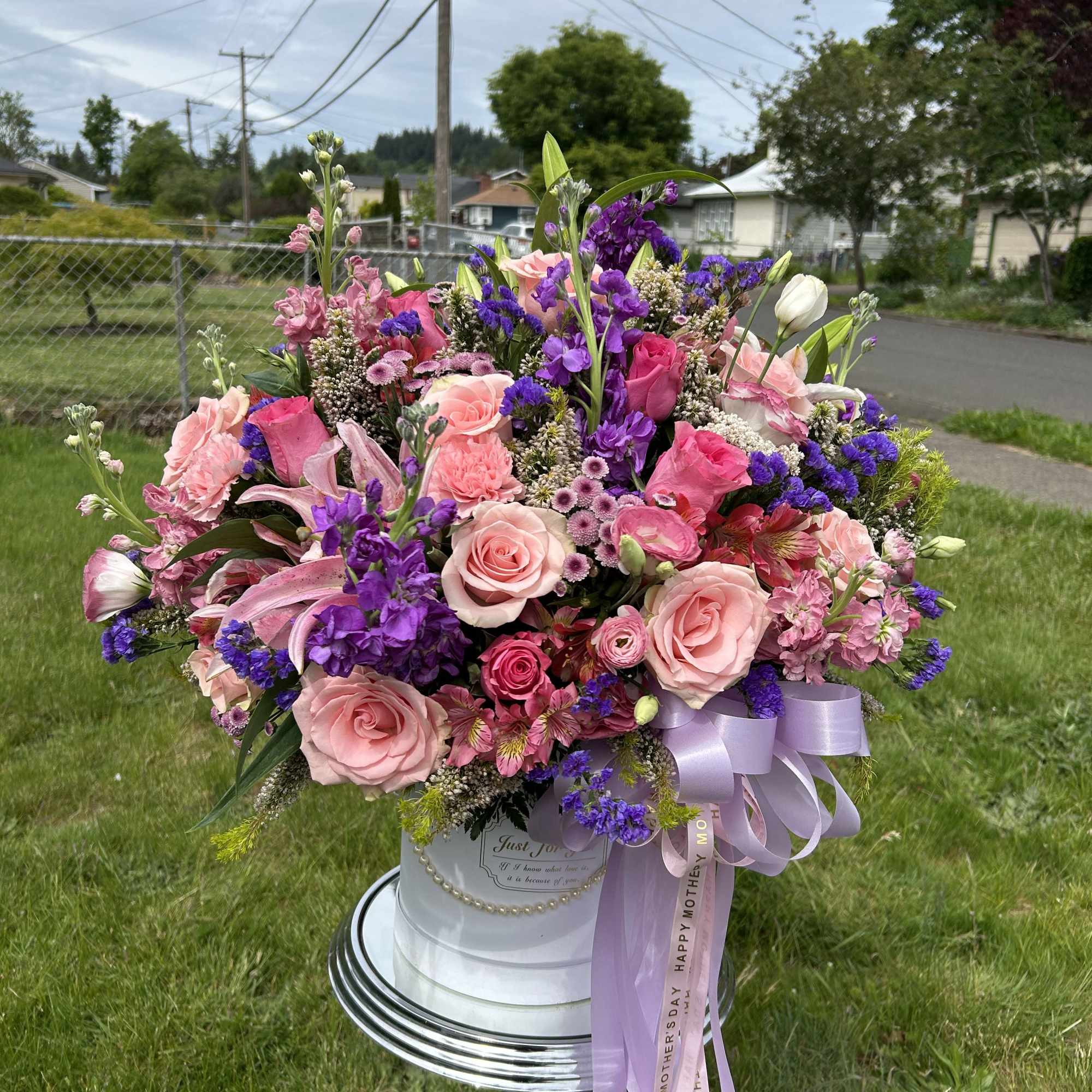 Large pink and purple flower arrangement in a white hatbox with lavender ribbon