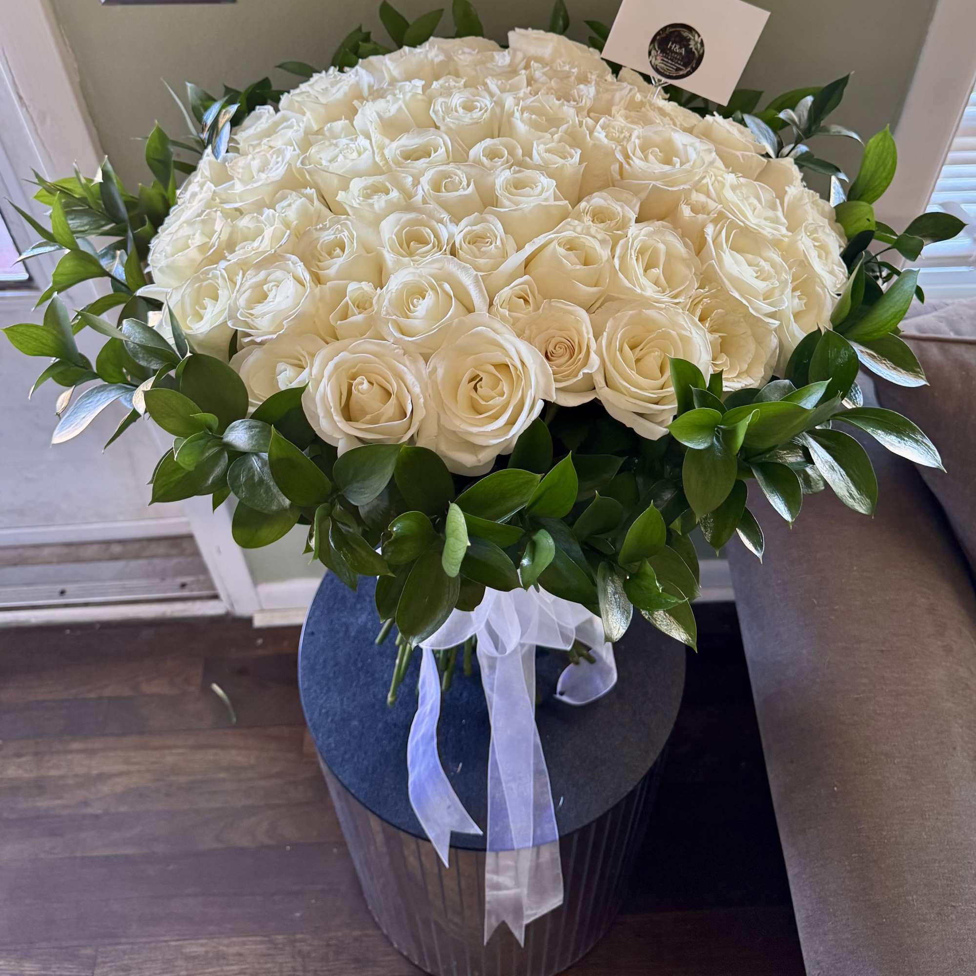 Large bouquet of white roses with a green leaf border and white ribbon