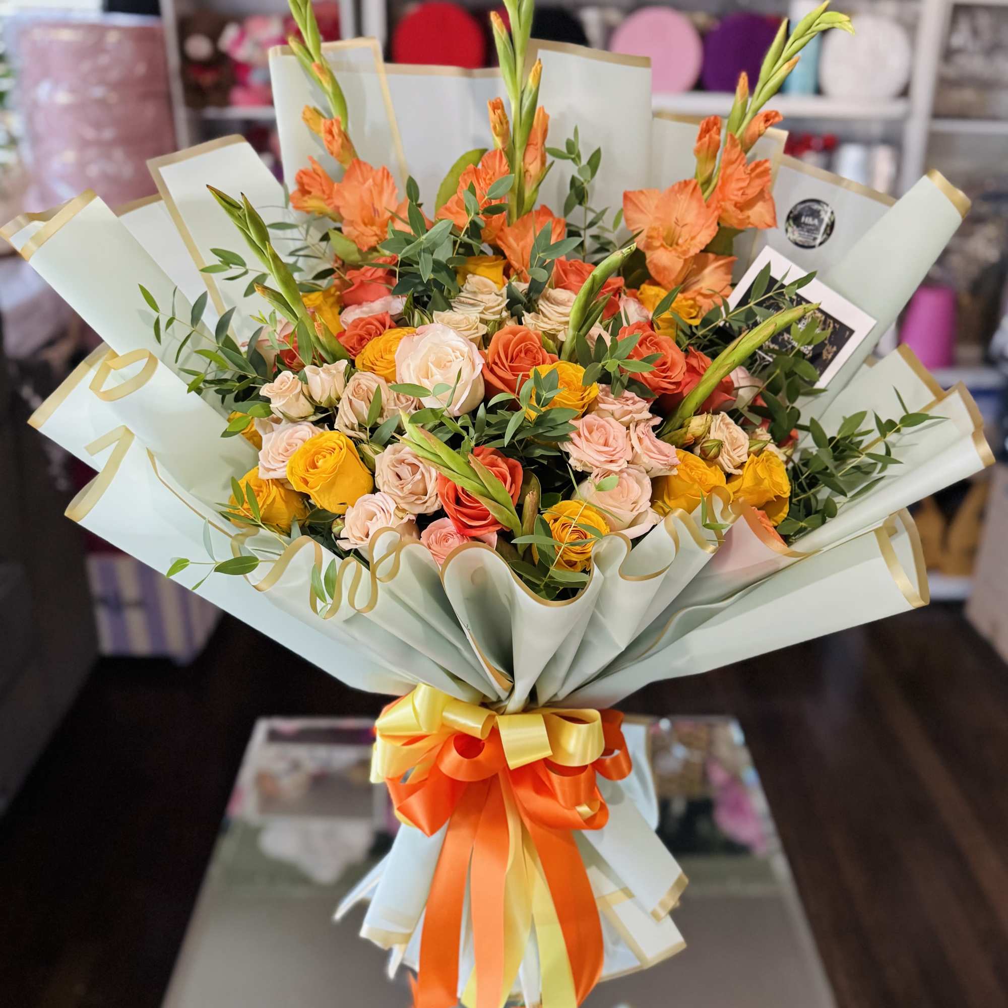 Bouquet of orange and peach roses with tall orange blooms wrapped in pale paper