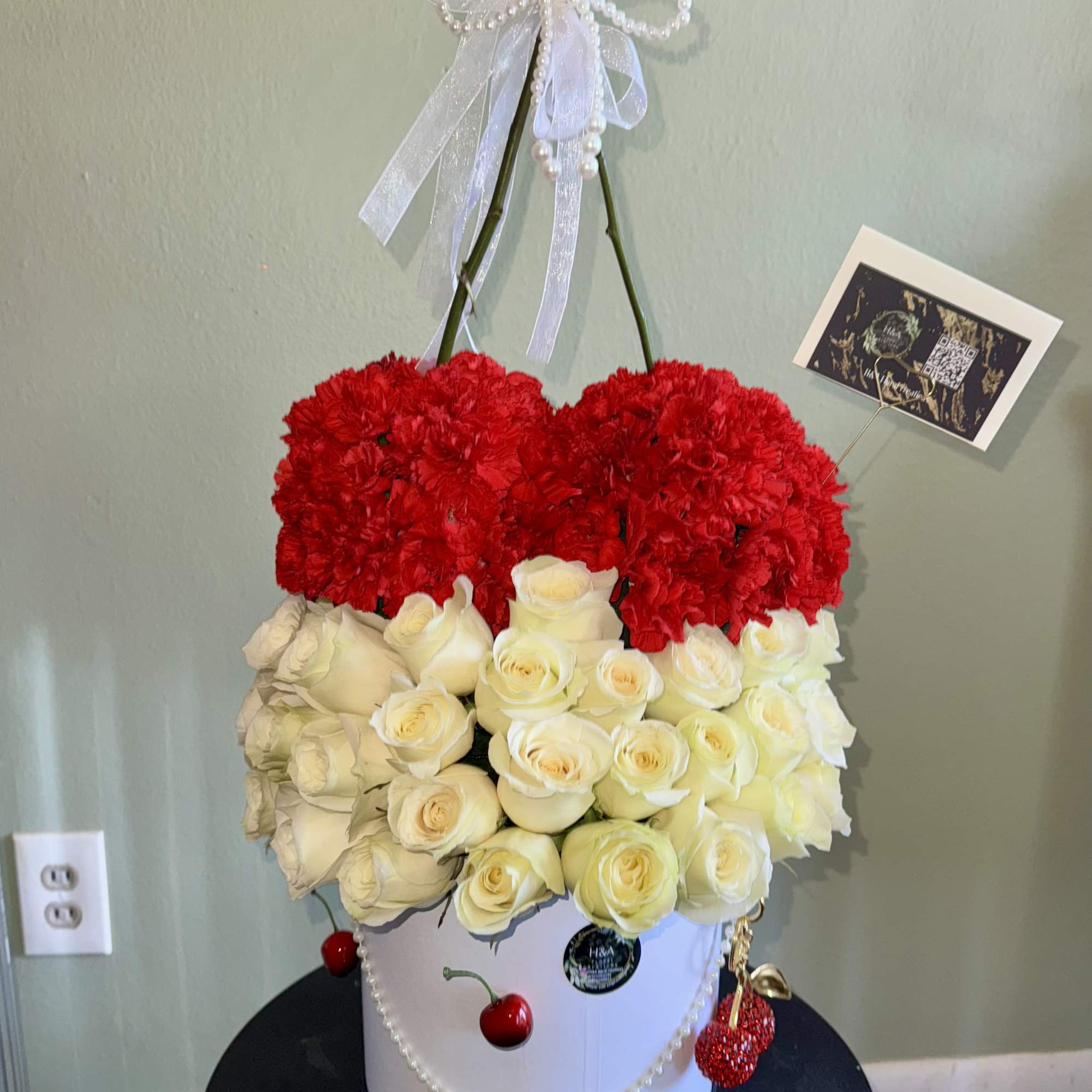 Heart-shaped red carnations above white roses in a white hatbox