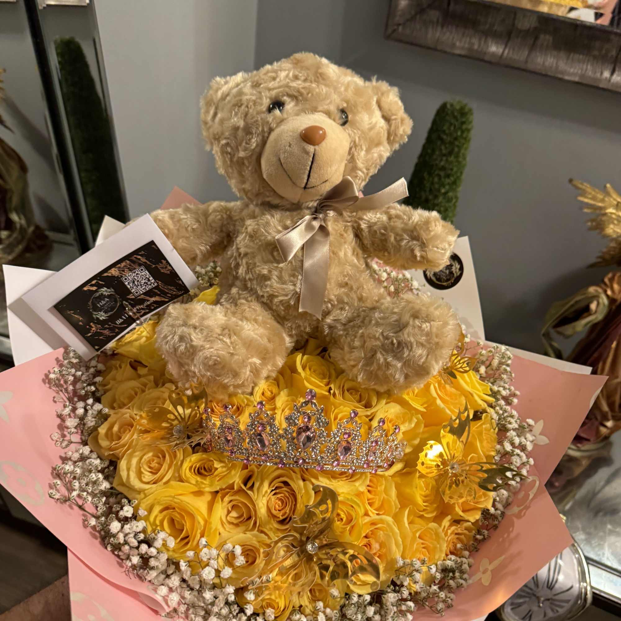 Teddy bear sitting on a bouquet of yellow roses with a tiara